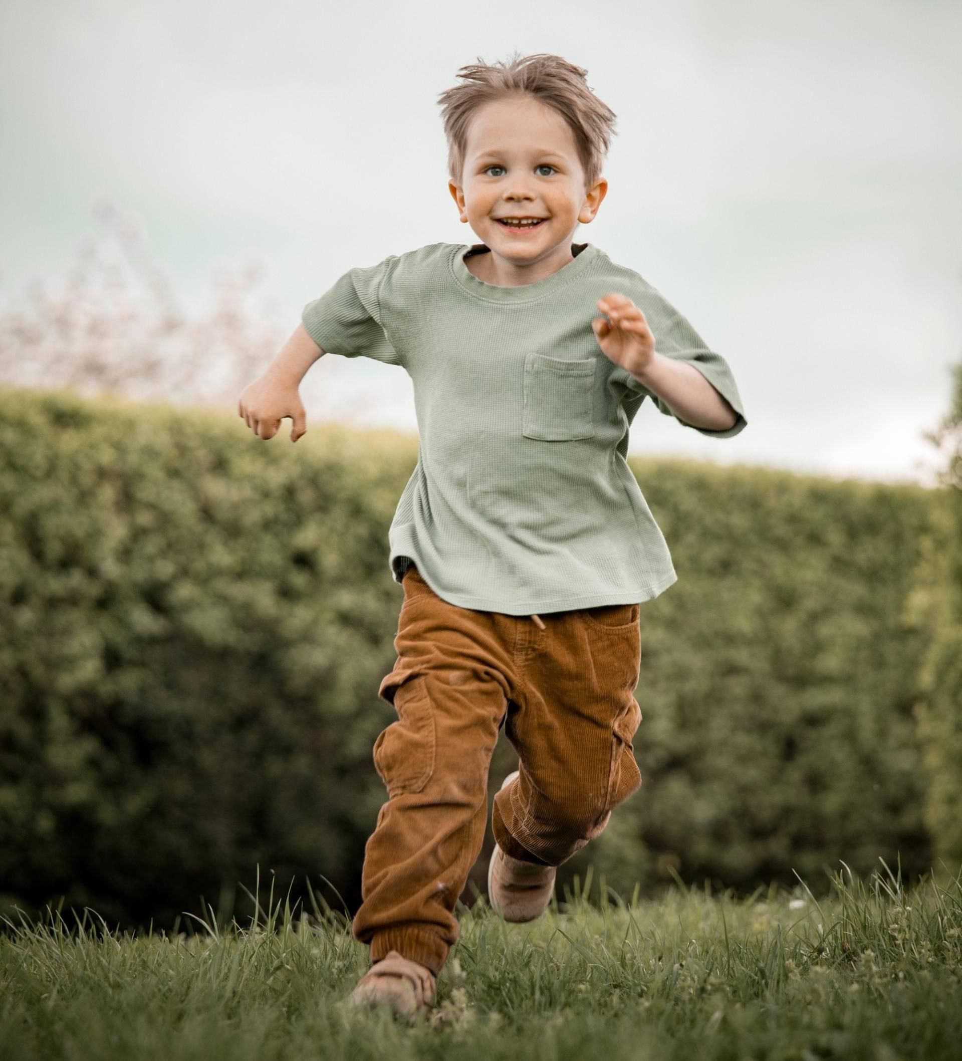 Kinderfotografie – Junge läuft lachend über die Wiese