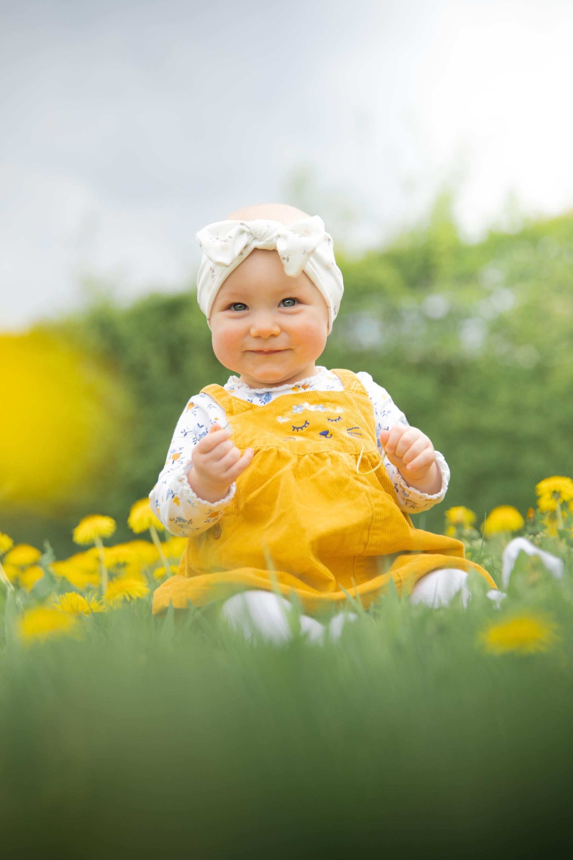 Kinderfotografie – lachendes Baby in gelbem Kleid im Grünen
