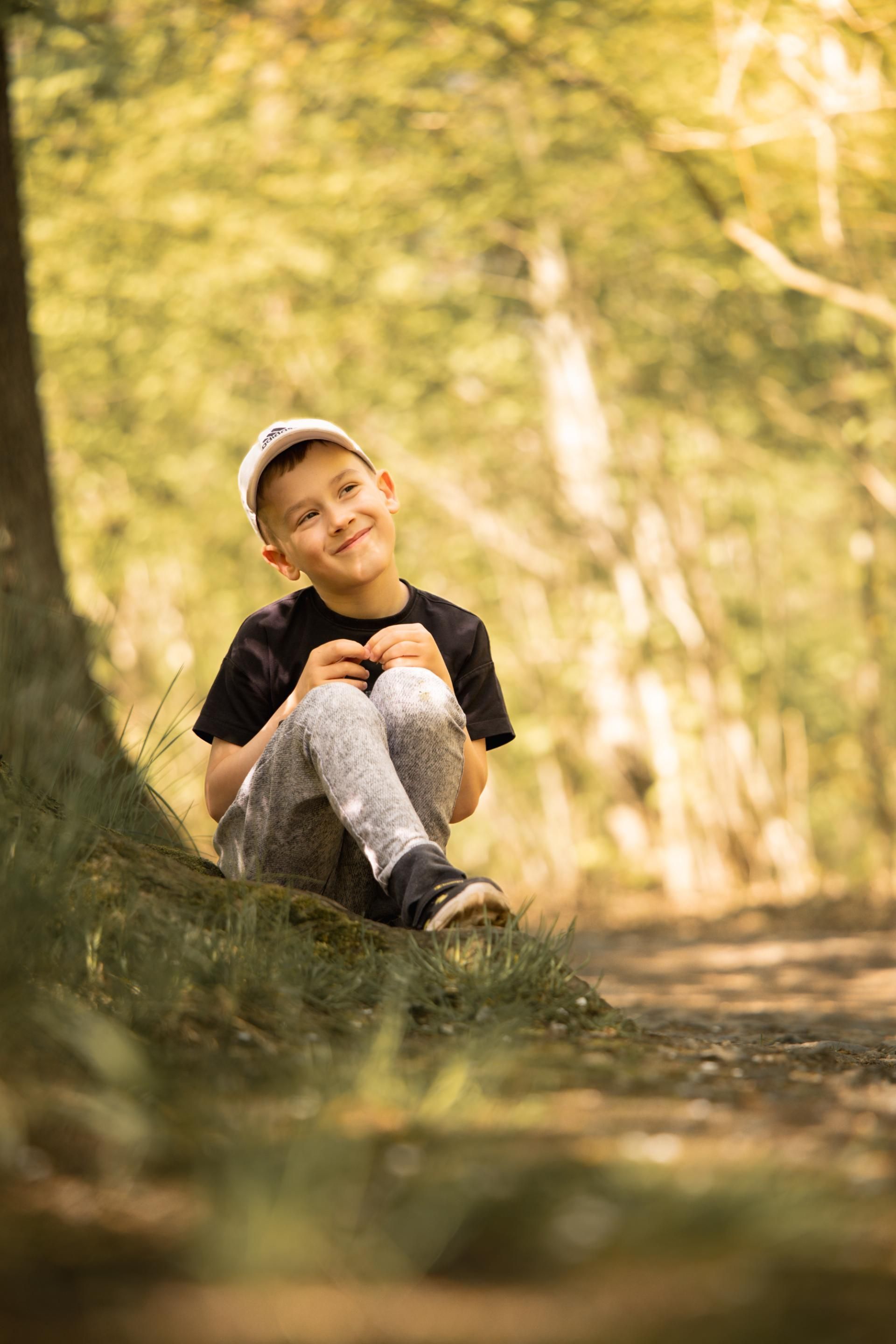 Kinderfotografie – Junge sitzt lachend auf einem Waldweg
