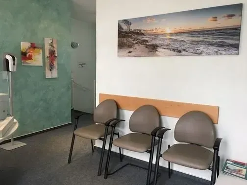 Ein Wartezimmer mit drei Stühlen und einem Gemälde an der Wand