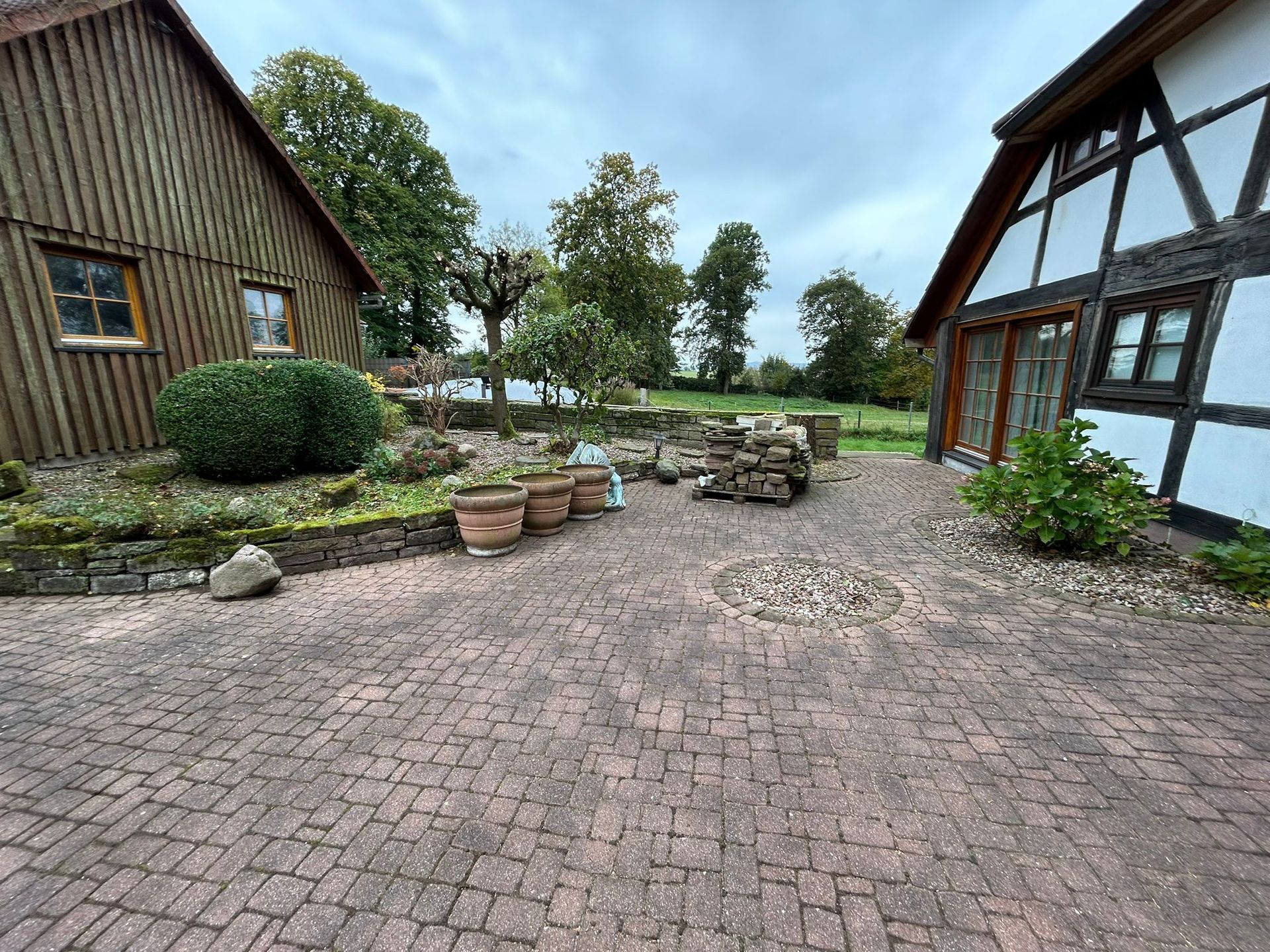 Eine gepflasterte Auffahrt führt zu zwei Häusern, davor stehen Topfpflanzen.