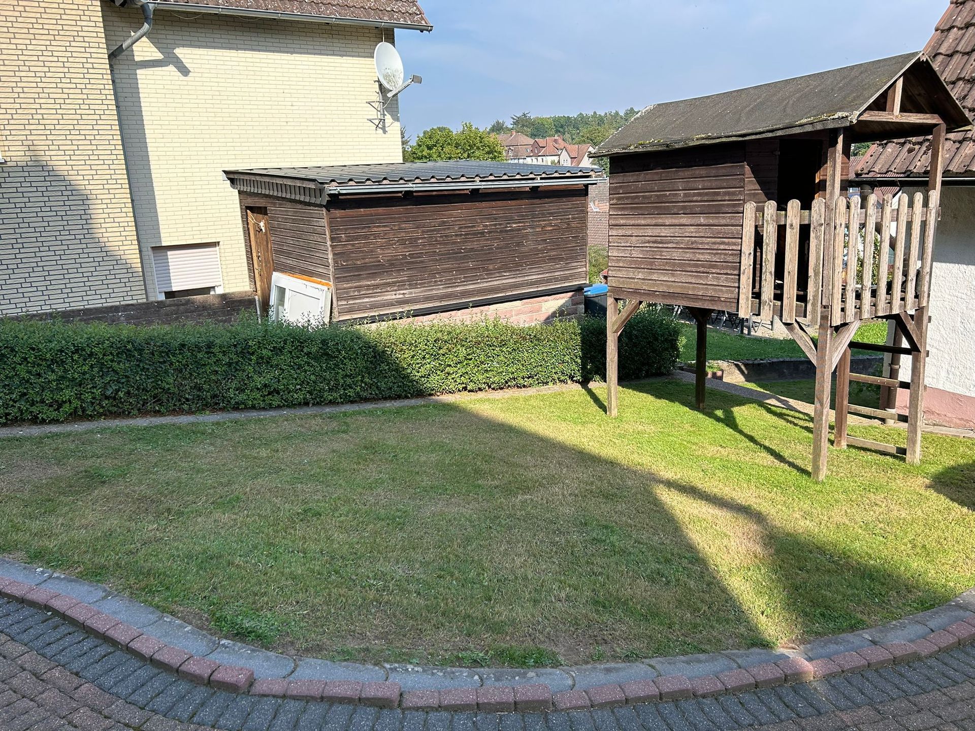 Ein hölzernes Spielhaus steht auf einem üppigen grünen Rasen vor einem Haus.