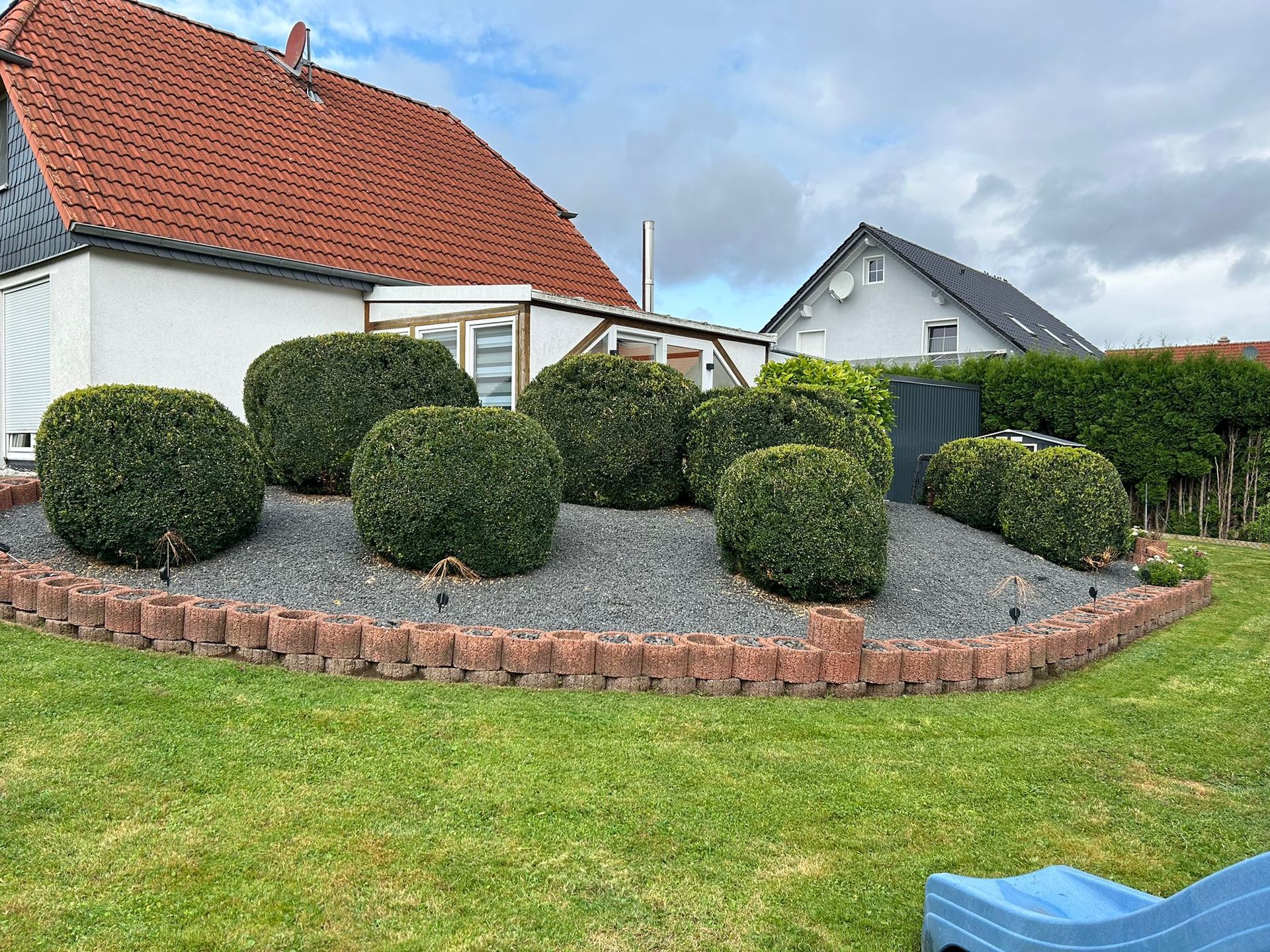 Ein Garten mit einem Haus im Hintergrund und einer blauen Rutsche im Vordergrund.