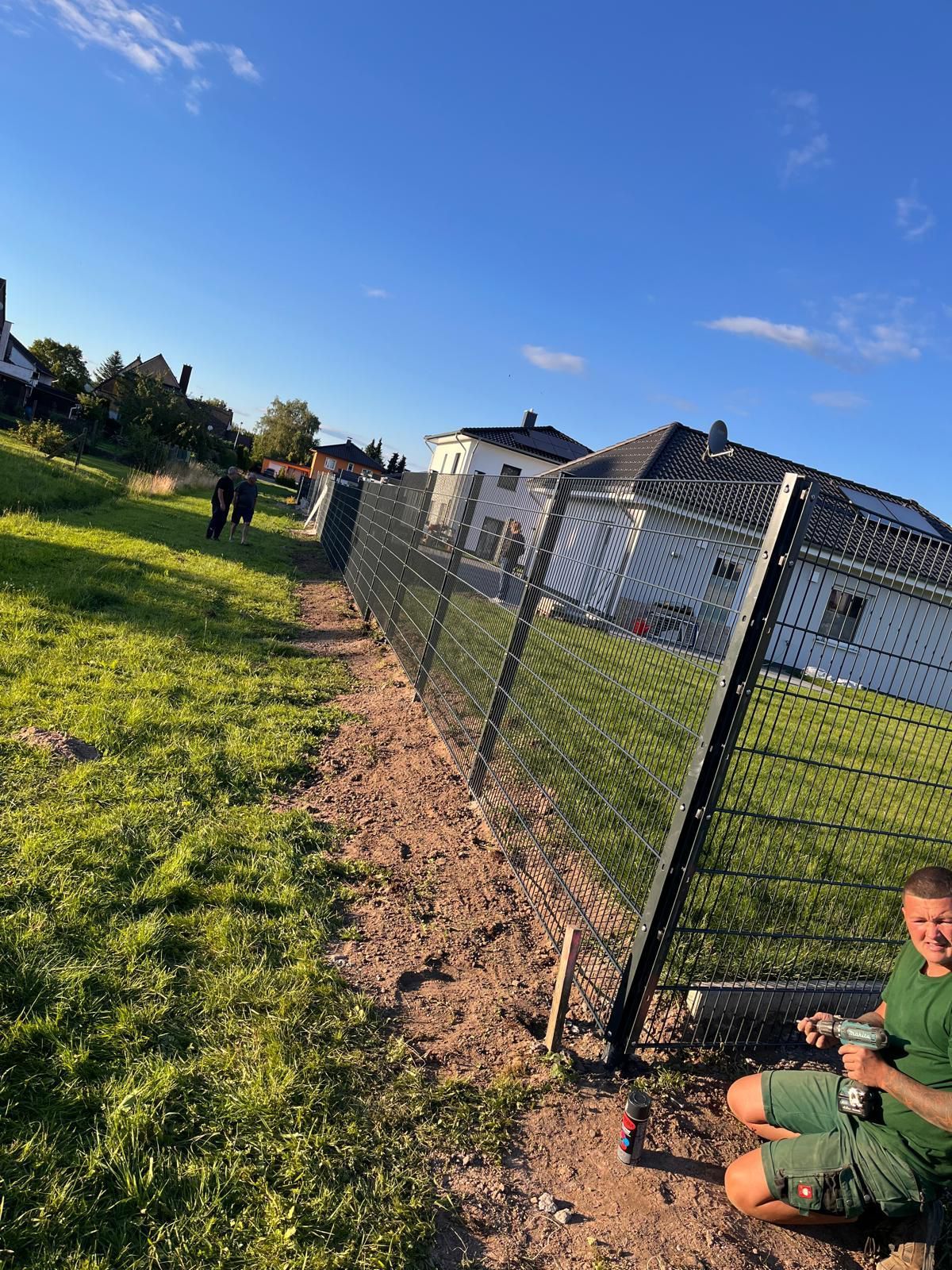 Ein Mann kniet neben einem Zaun auf einem Feld.