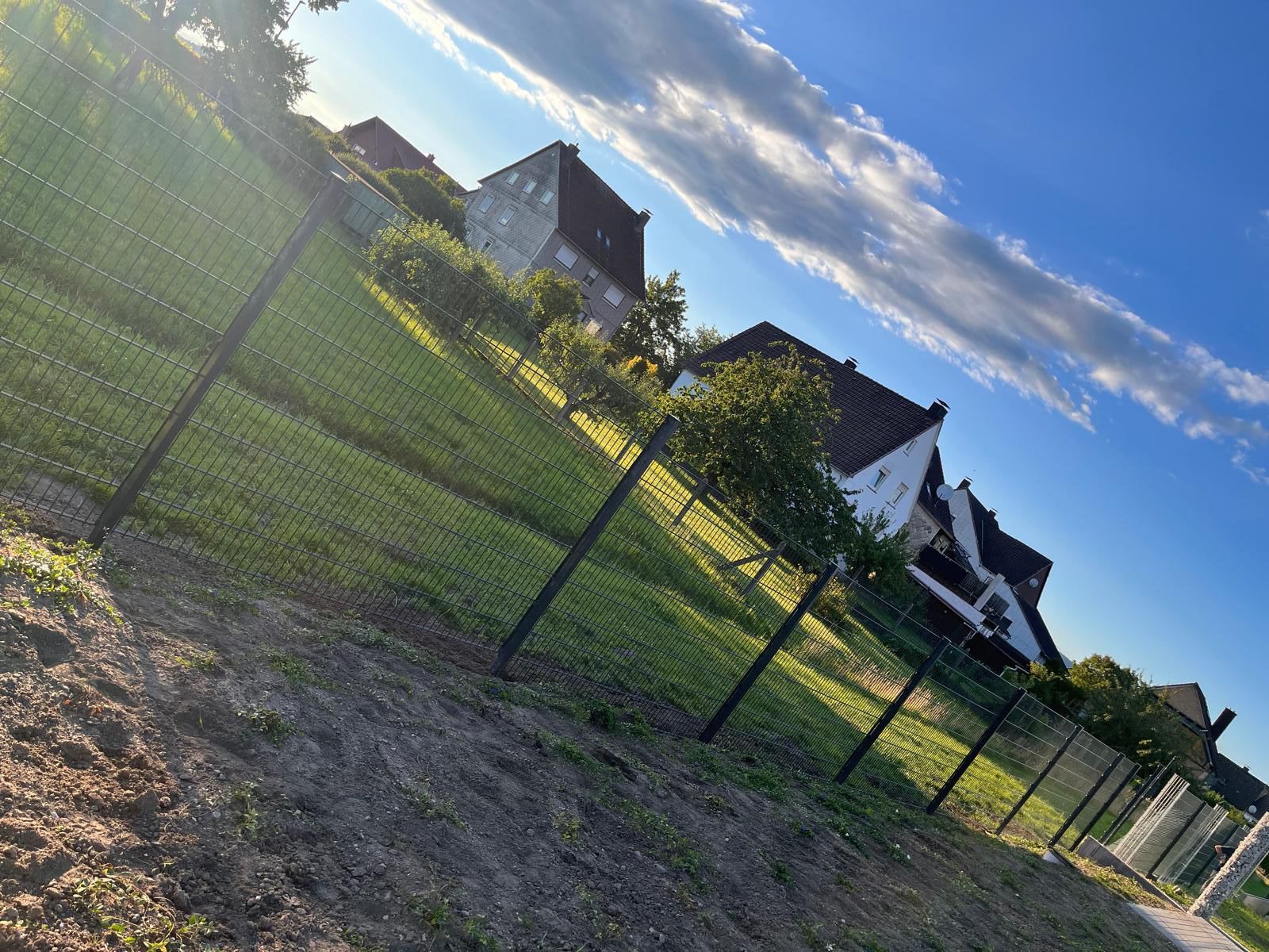 Ein Zaun umgibt ein üppiges grünes Feld mit Häusern im Hintergrund.