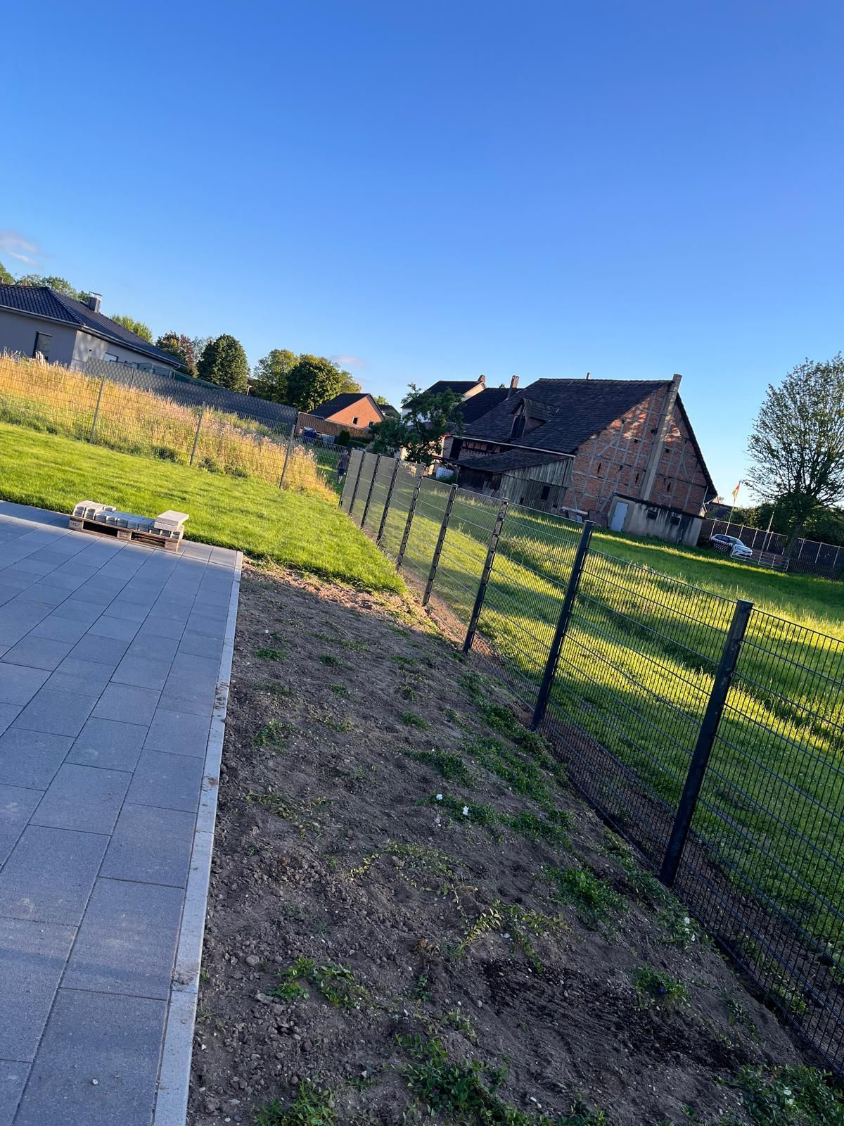 Ein Zaun umgibt eine Wiese mit einem Haus im Hintergrund.