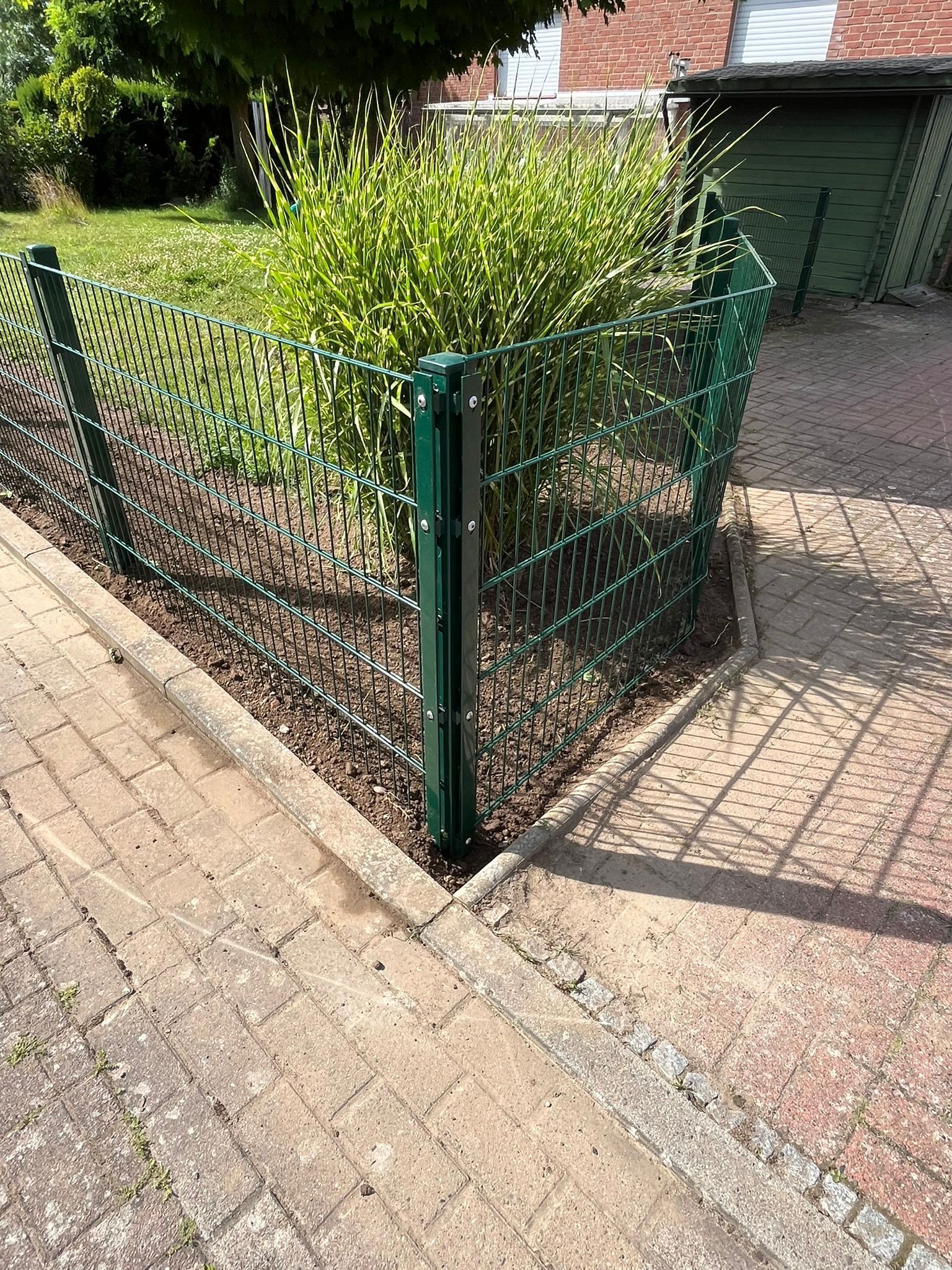 Am Rand einer Backsteinstraße steht ein grüner Zaun.