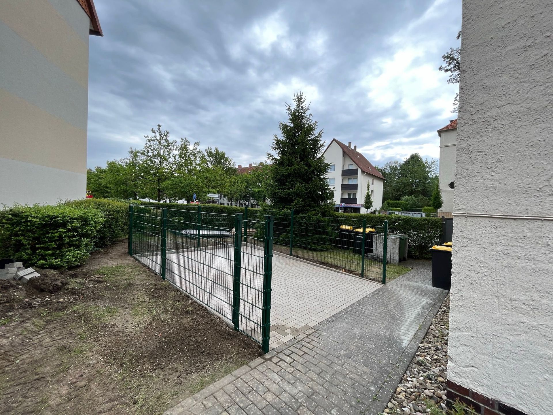 Ein Zaun umgibt einen Backsteinweg vor einem Gebäude.