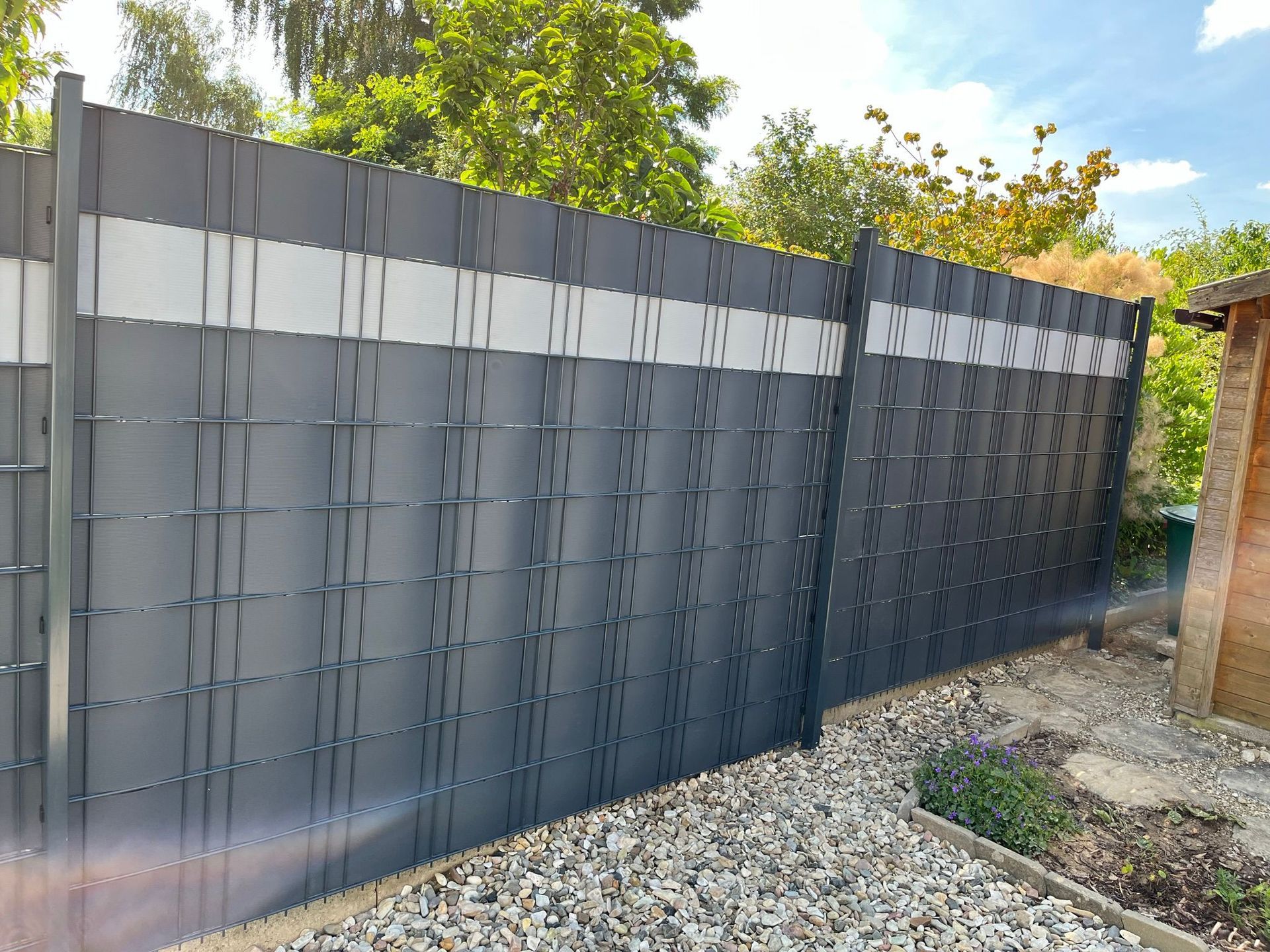 Ein schwarzer Zaun mit einem weißen Streifen an der Seite ist von Kies umgeben.