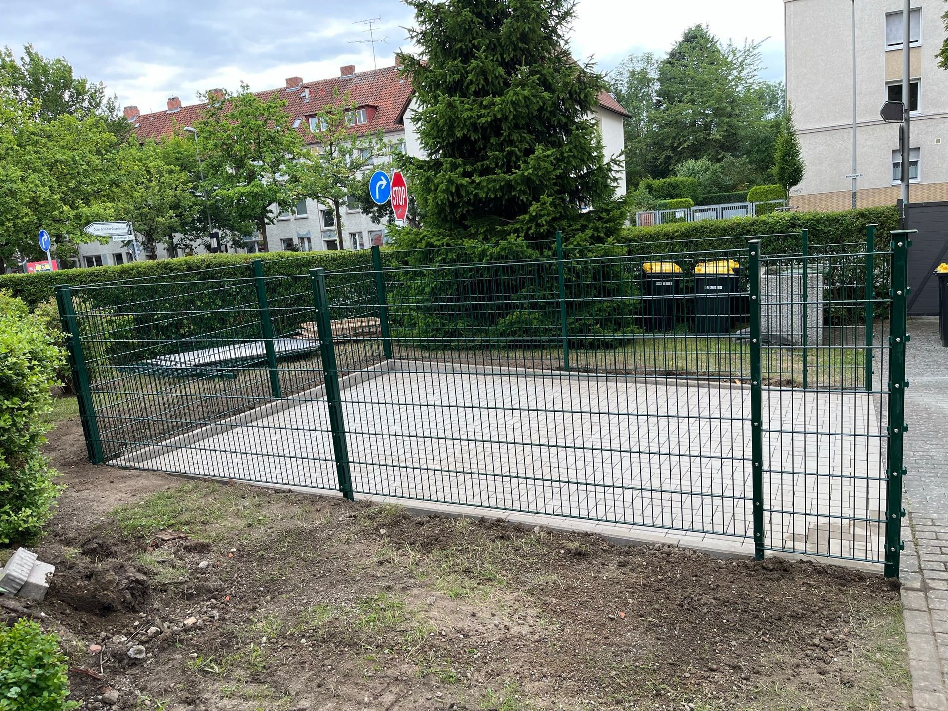 Ein grüner Zaun umgibt einen Backsteinweg in einem Park.