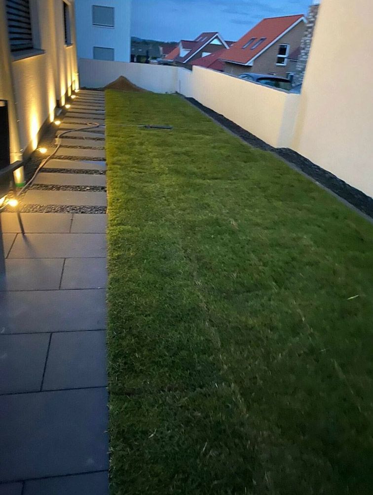 Ein Gehweg, der zu einem üppigen grünen Rasen mit Häusern im Hintergrund führt.