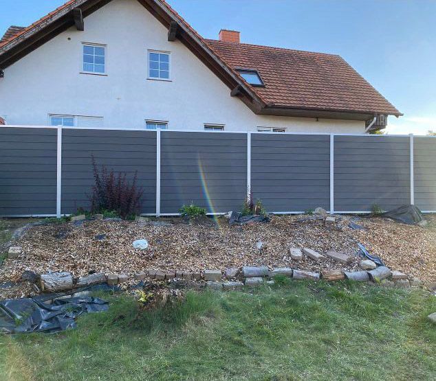 Ein weißes Haus mit einem grauen Zaun davor.