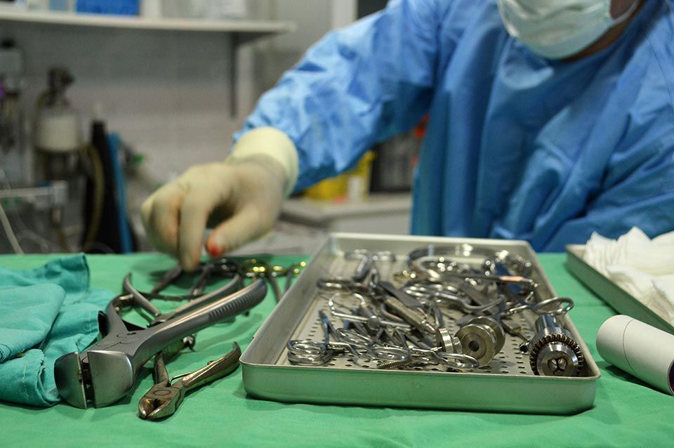Un cirujano está trabajando en una bandeja de instrumentos quirúrgicos sobre una mesa.