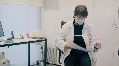 Un médico que lleva una máscara está sentado en una silla sosteniendo un trozo de papel.