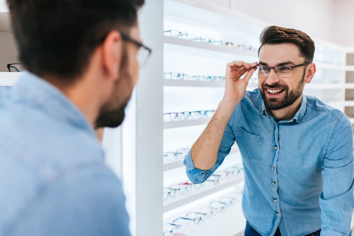 Un hombre se prueba unas gafas frente a un espejo en una óptica.