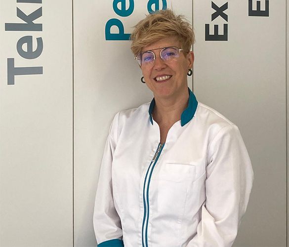 Una mujer con bata de laboratorio sonríe delante de un microscopio.