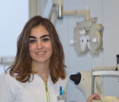 Una mujer con bata de laboratorio sonríe delante de un microscopio.