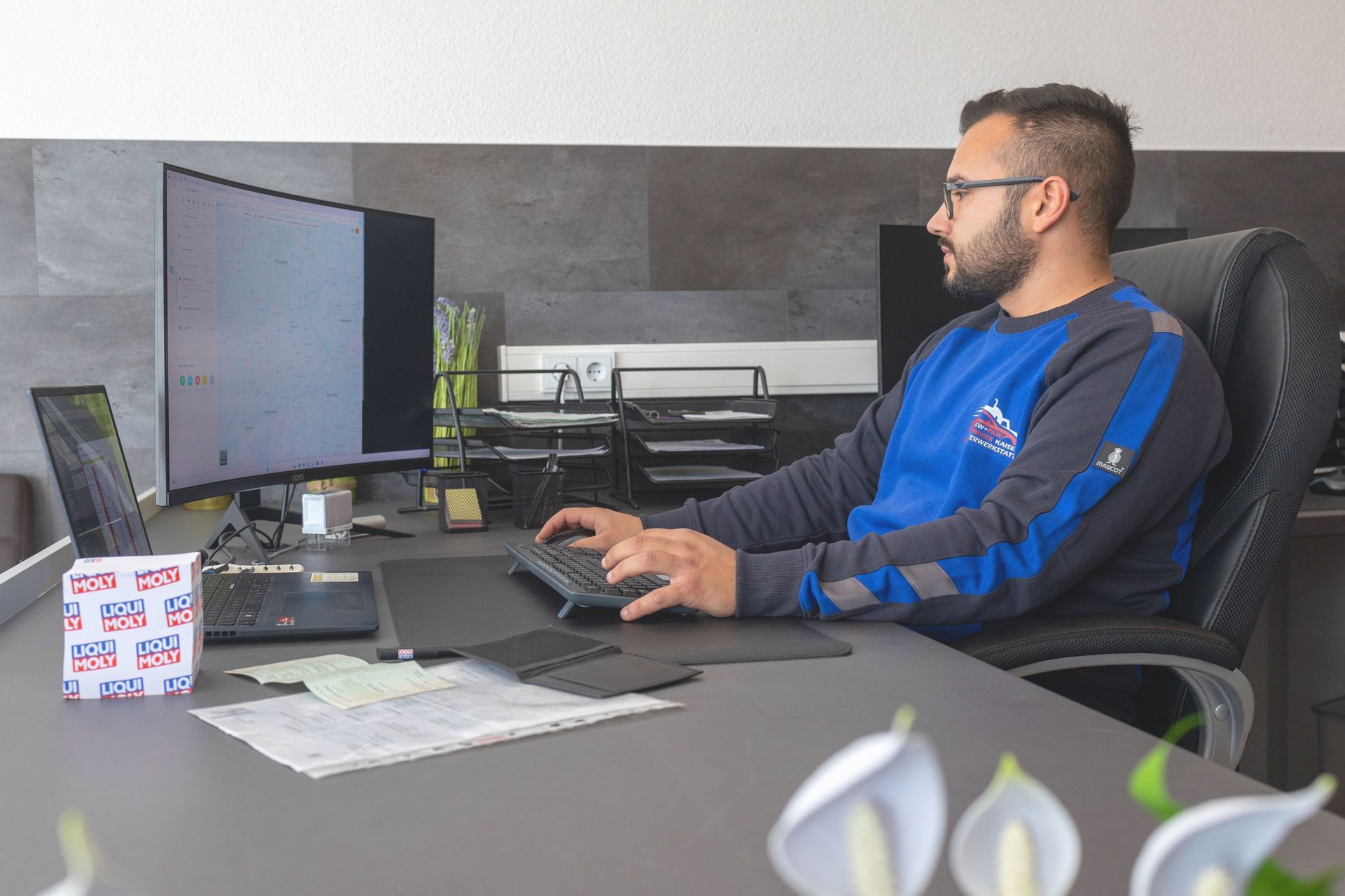 Ein Auto wird in einer Werkstatt mit geöffnetem Kofferraum repariert.