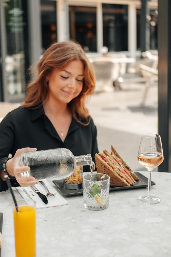 Vrouw schenkt water in in een restaurant, met eten en drinken erbij.