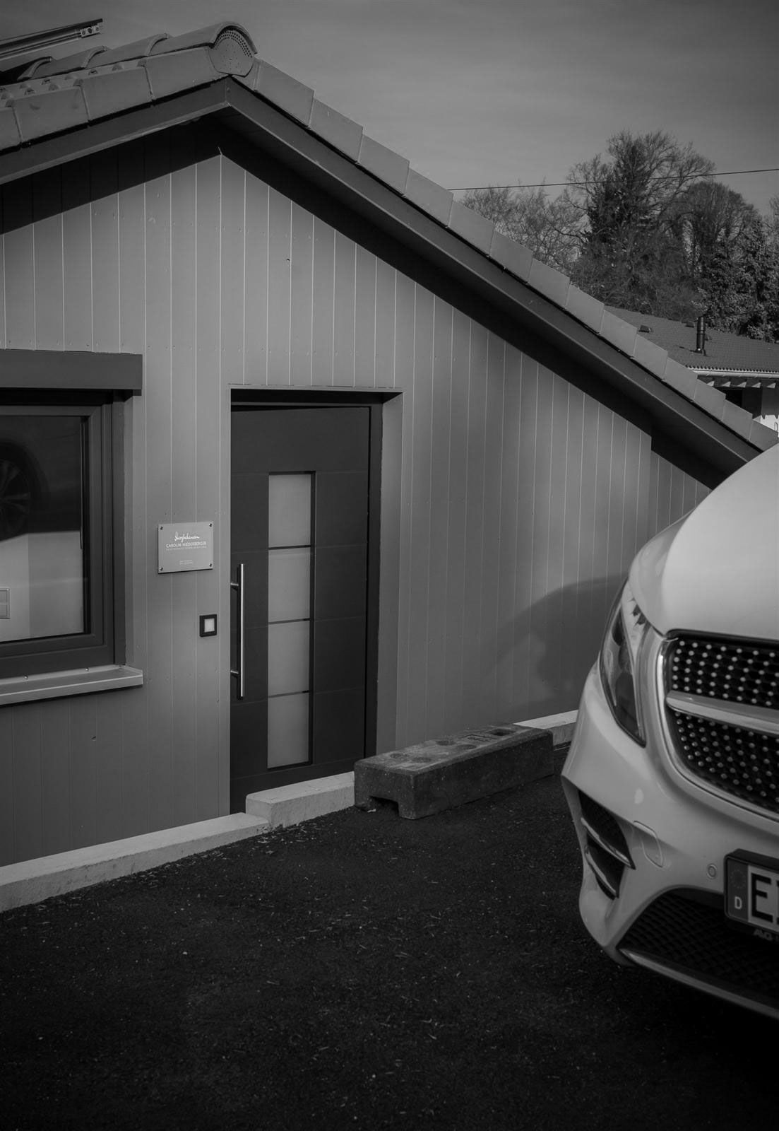 Ein Schwarzweißfoto eines vor einem Haus geparkten Autos.