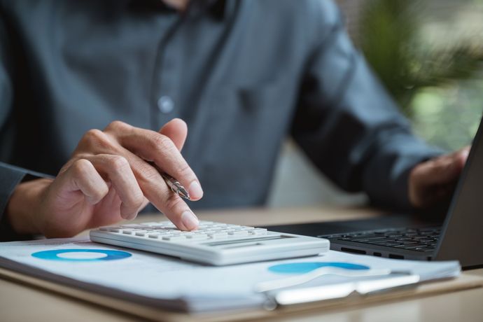 Person, die einen Taschenrechner und einen Laptop über Finanzdokumenten mit Kreisdiagrammen verwendet.