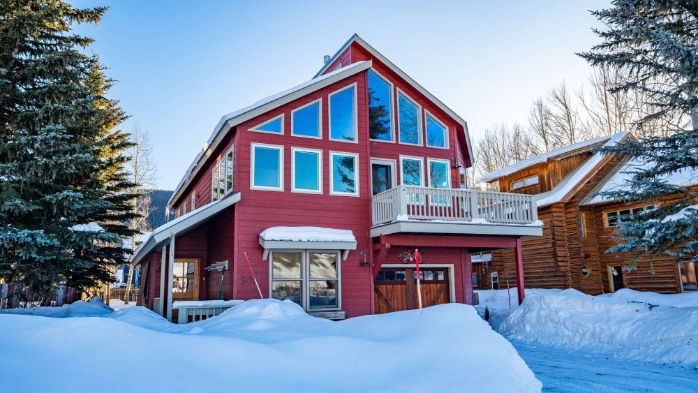 Red house with large windows in a snowy setting; garage and small balcony.