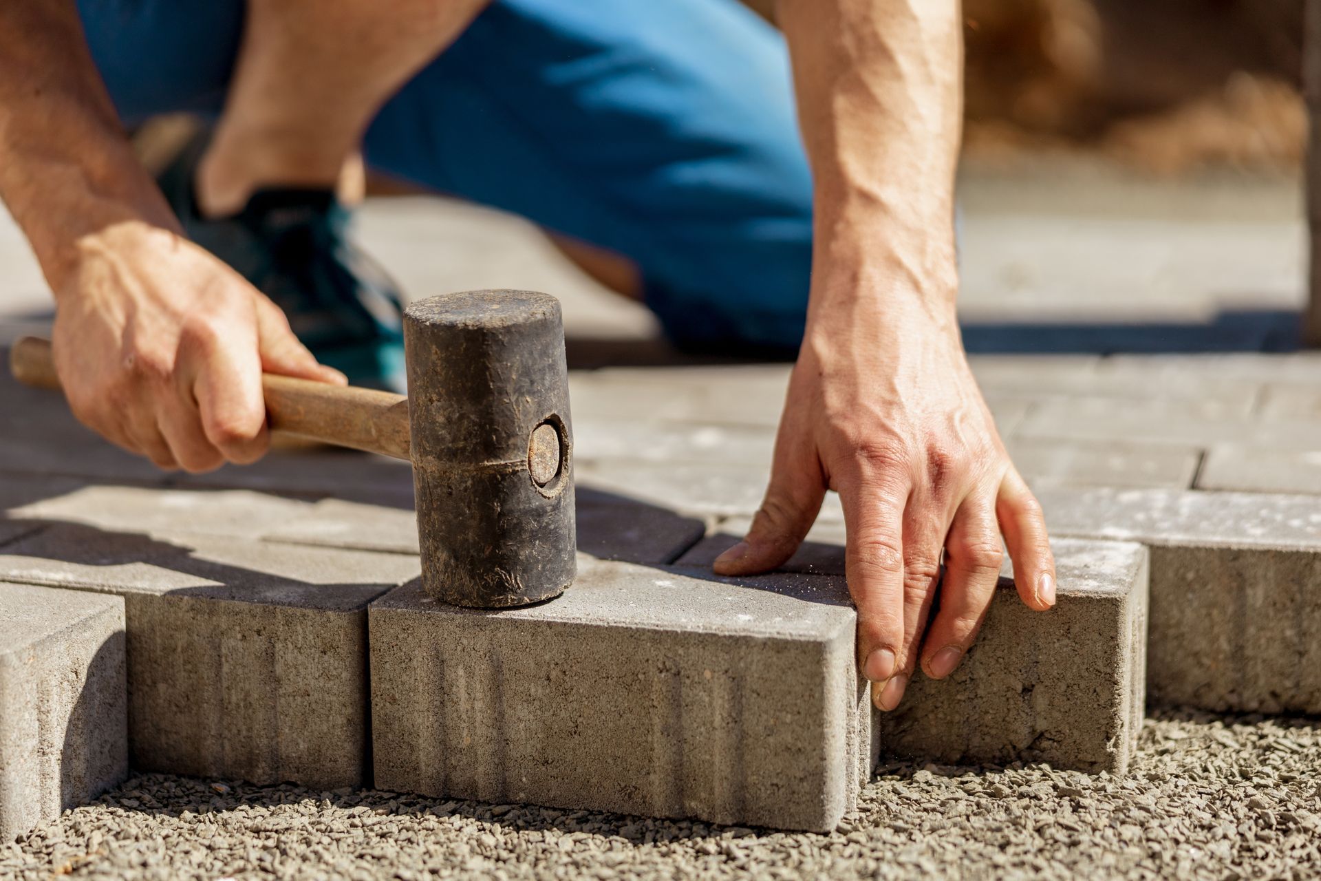 Main avec marteau tapant sur un pavé