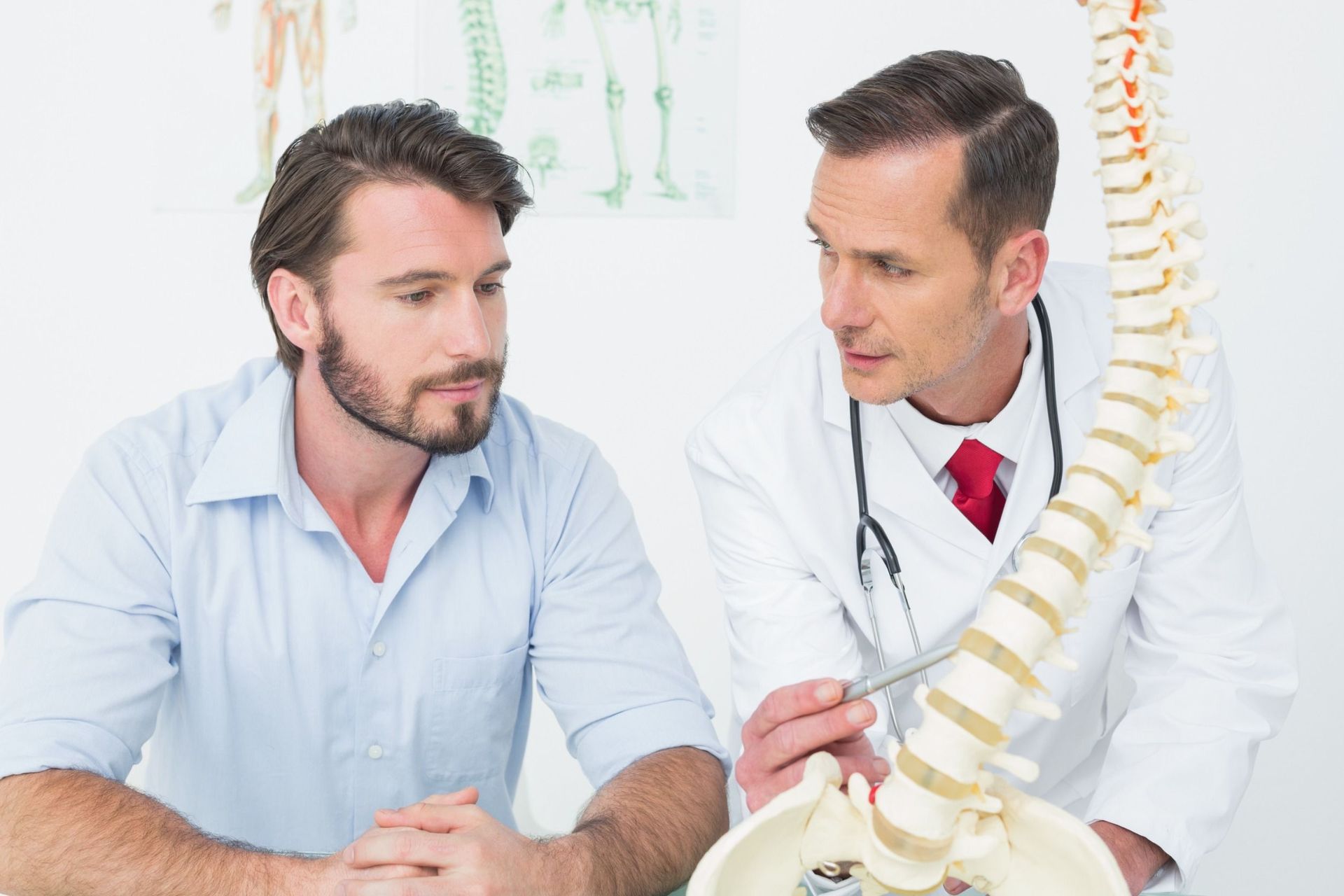 Un médico y un paciente miran un modelo de una columna vertebral.