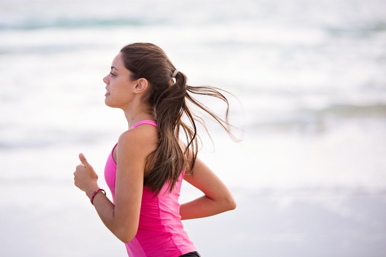 Una mujer con una camiseta rosa corre por la playa.