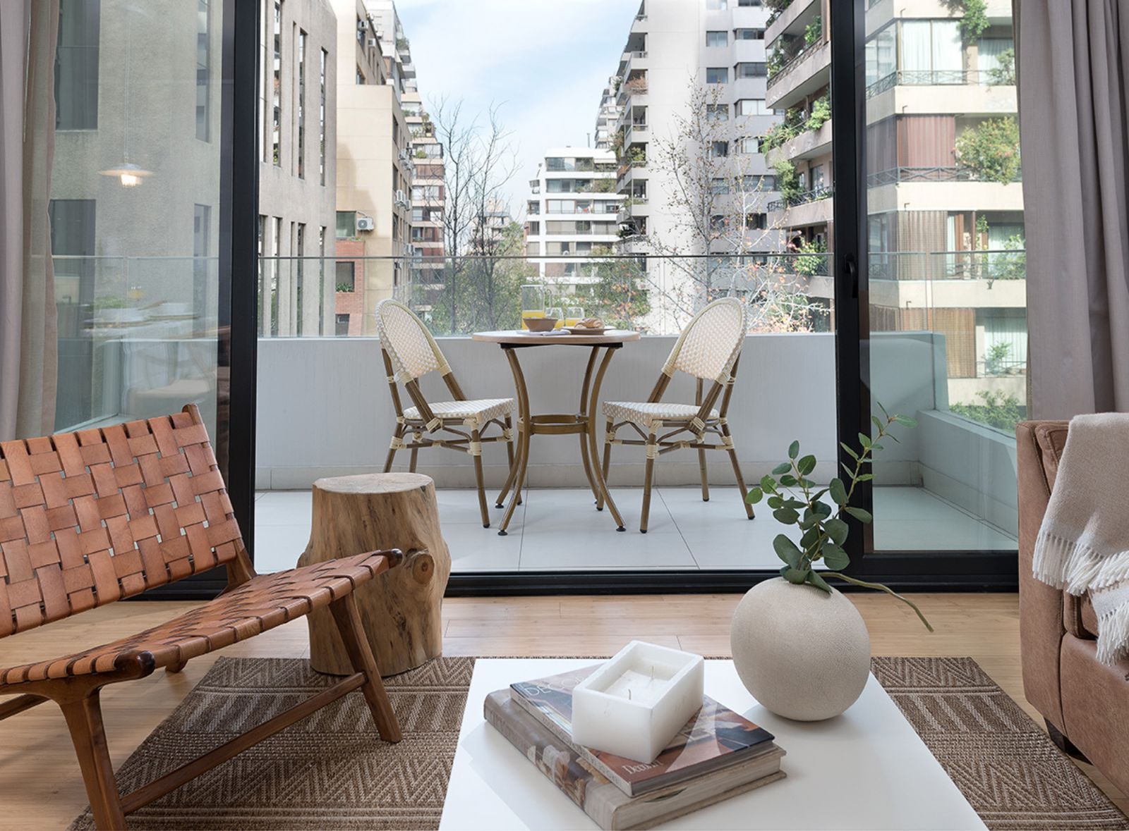Modern balcony with wicker chair, small table, and potted plant overlooking apartment buildings.
