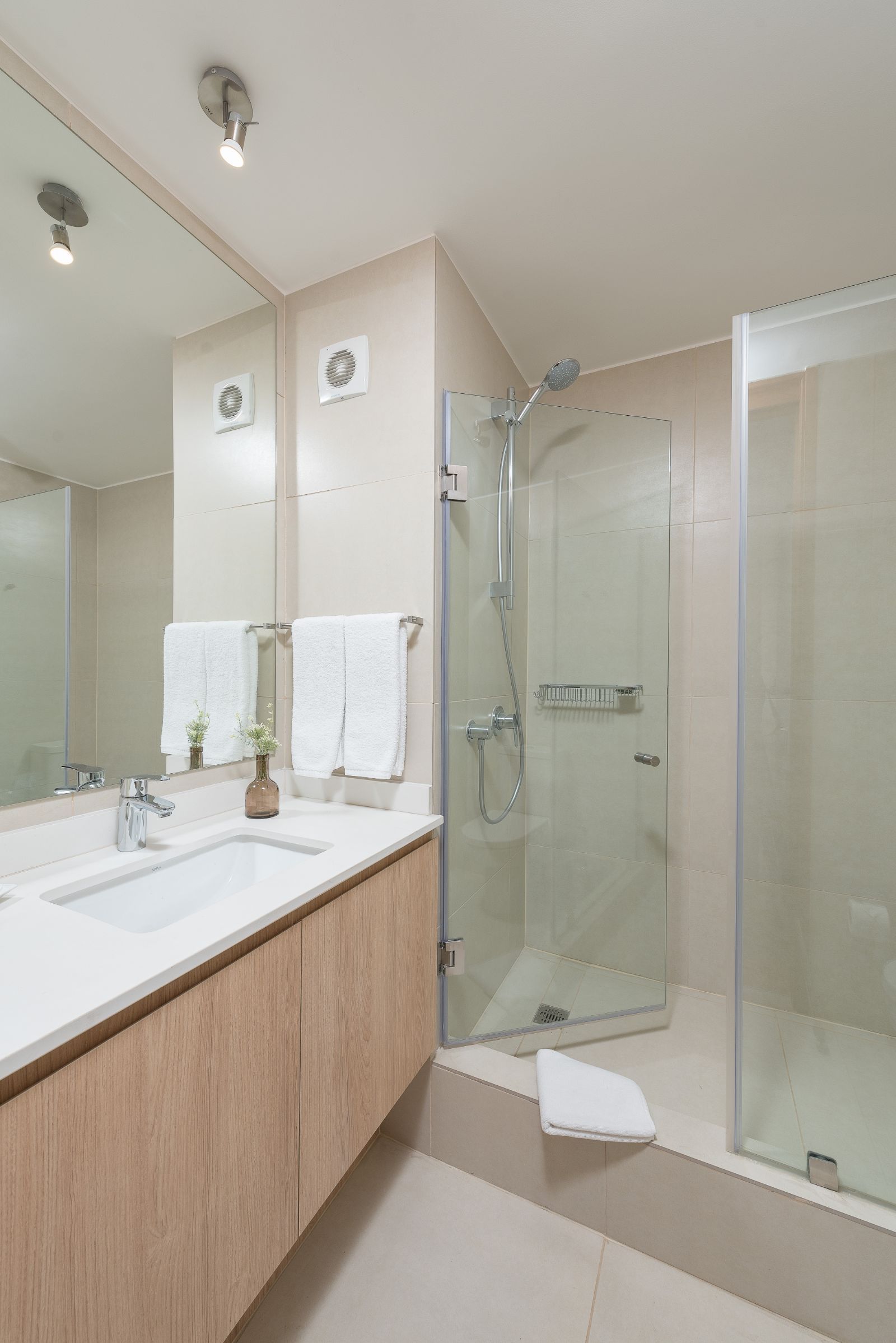 Modern bathroom with double vanity, large mirror, and glass shower enclosure