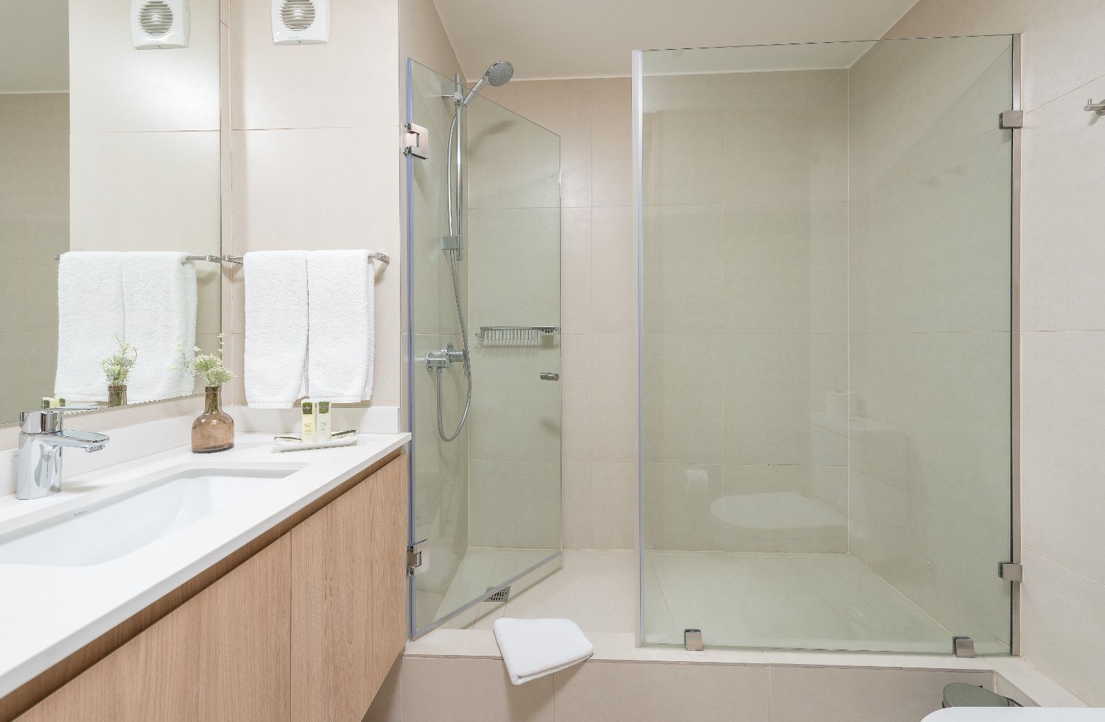 Modern bathroom with double vanity, glass shower, and neutral beige tile.