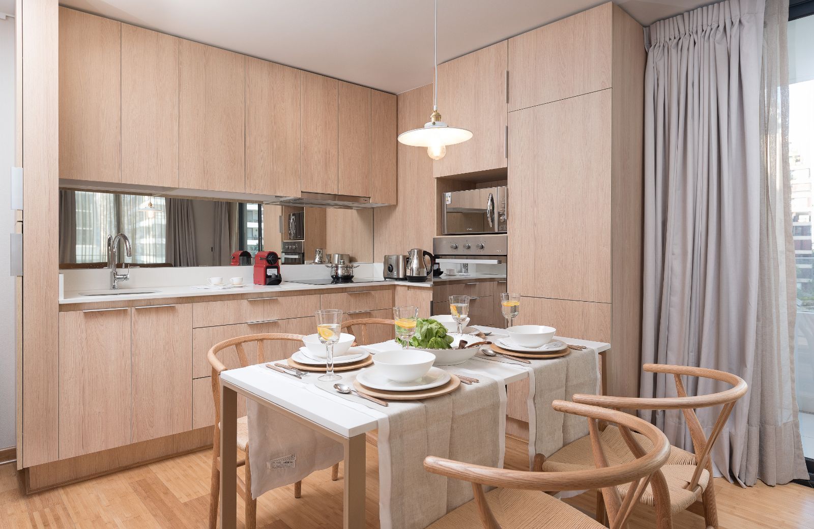 Modern kitchen and dining area with light wood cabinets, a white table set for four, and wooden chairs