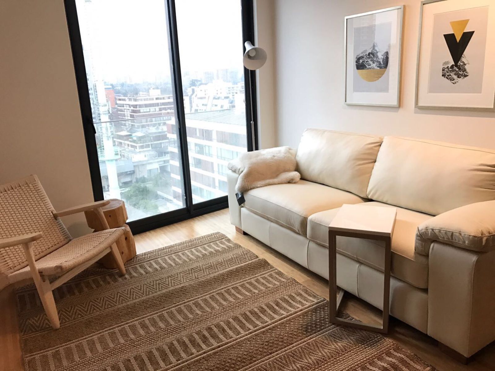 Cozy living room with beige sofa, wicker chair, rug, wall art, and large window city view