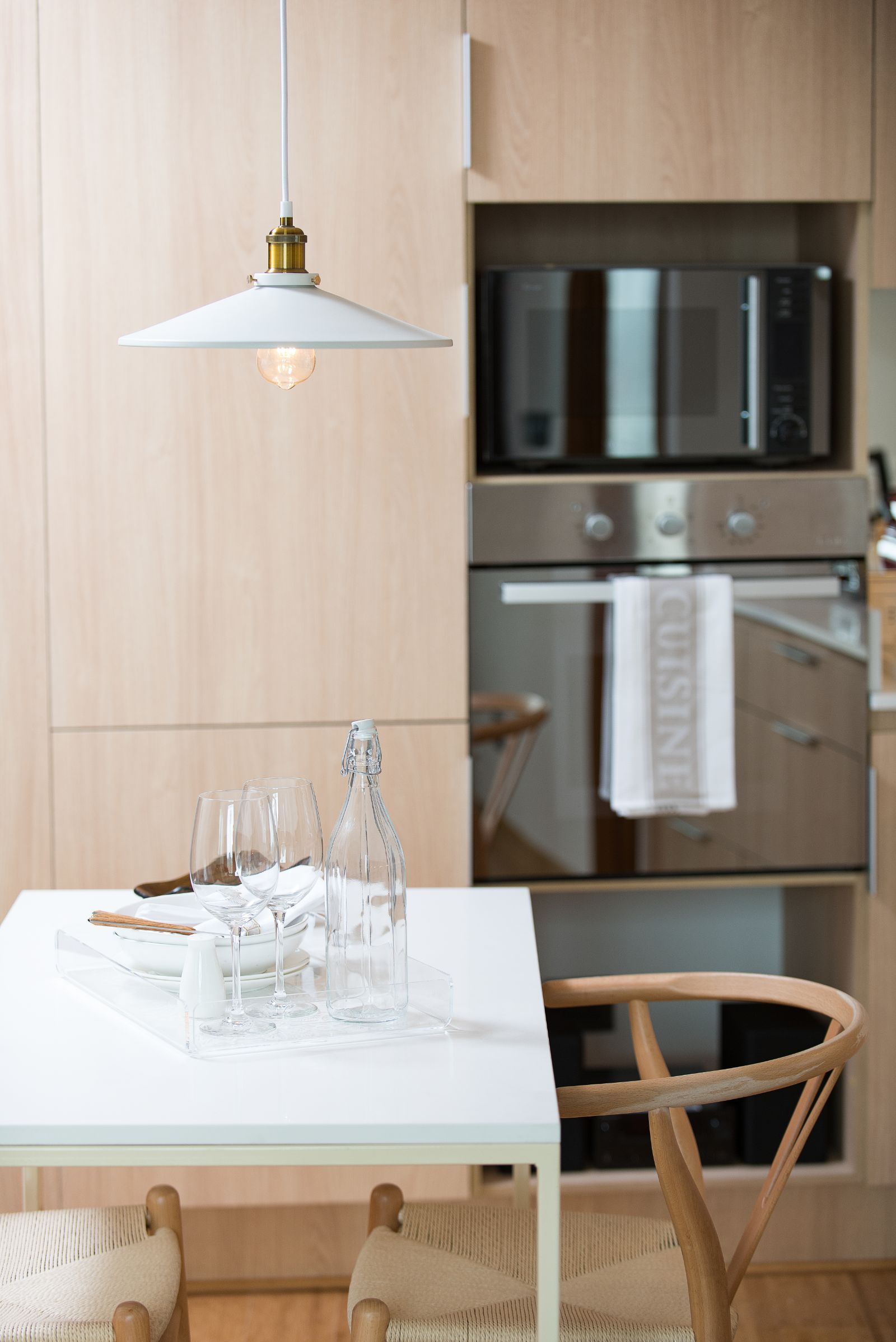 Modern kitchen-dining nook with white table, hanging lamp, and built-in oven and microwave.