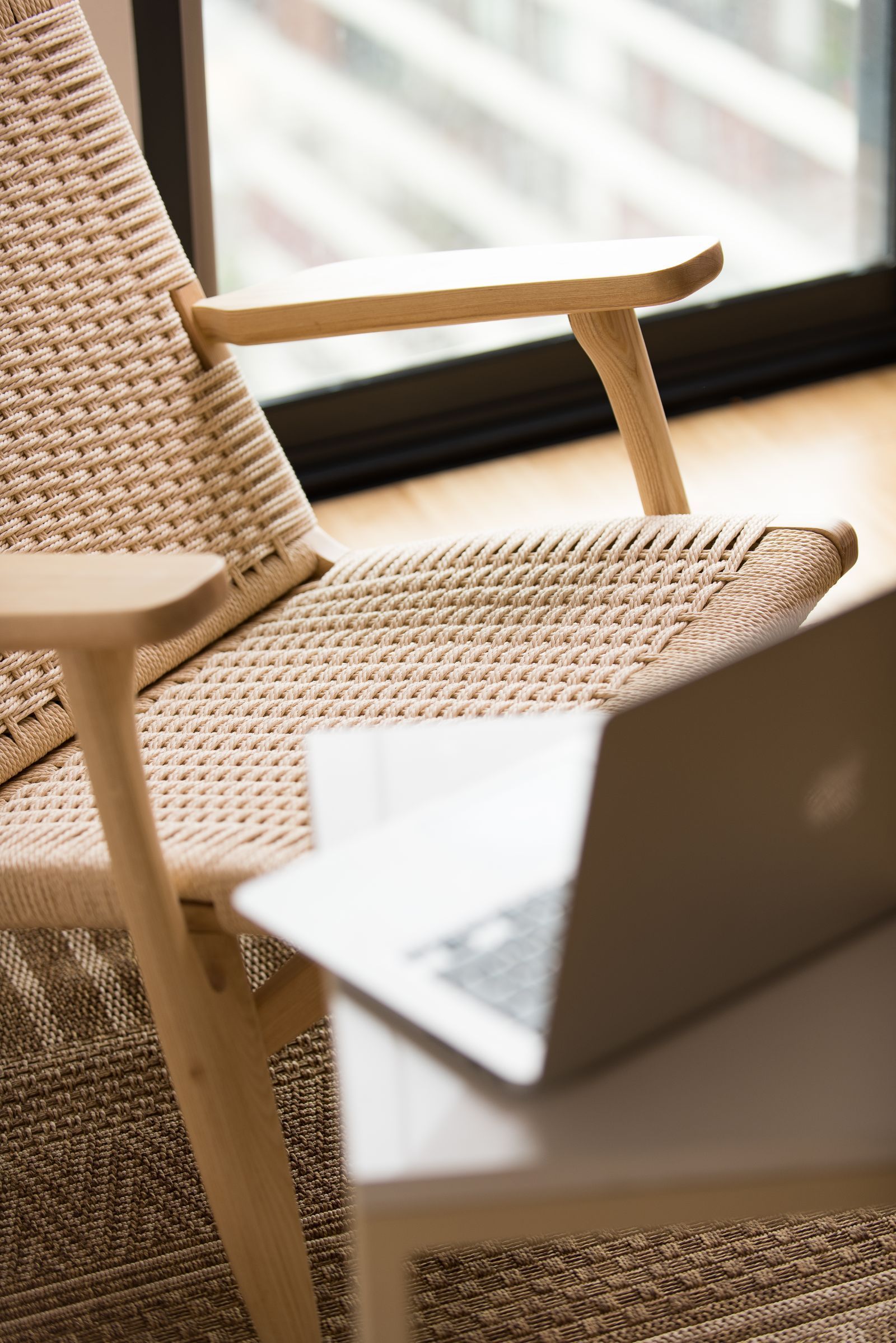 Woven chair beside a laptop near a sunlit window