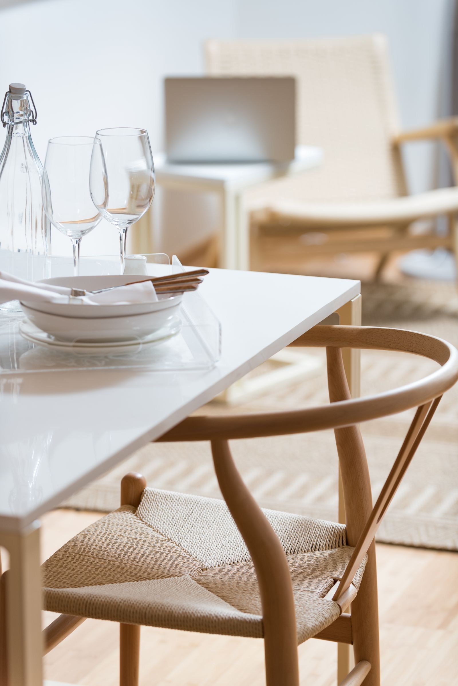 Bright dining table with woven chairs, glassware, and a blurred chair in a sunlit room