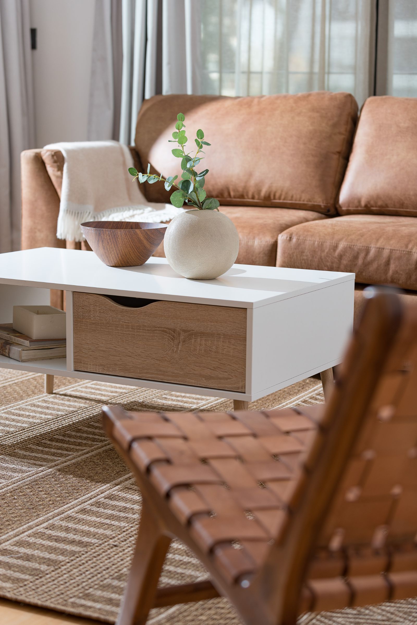 Cozy living room with a tan sofa, white coffee table, woven chair, and woven rug