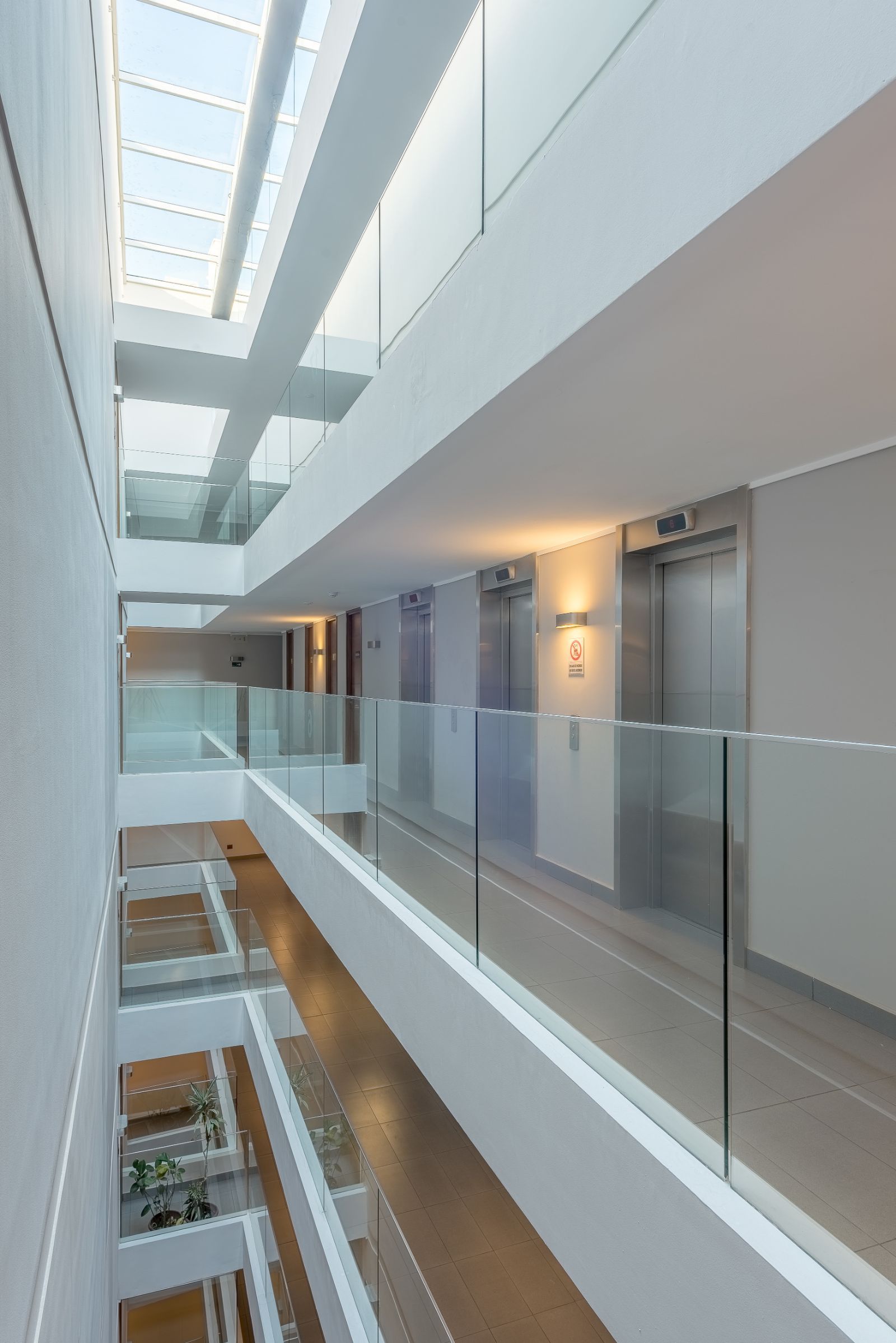 Modern office atrium with glass railings, skylight, and corridor doors on upper floors