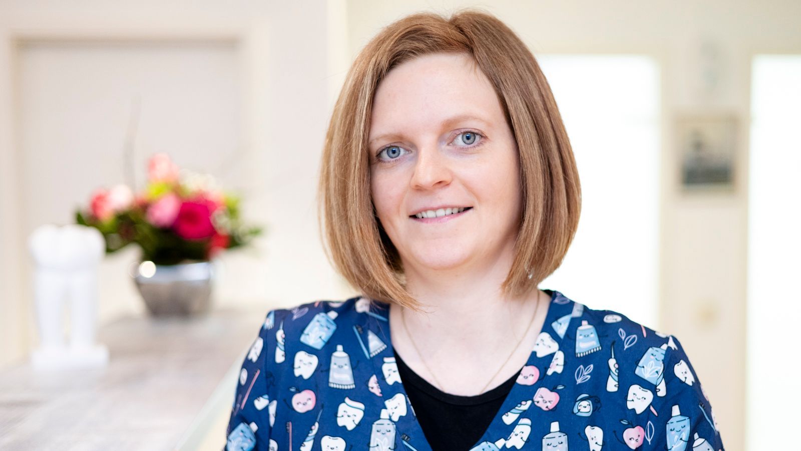 Eine Frau in einem blauen OP-Kittel lächelt in die Kamera.