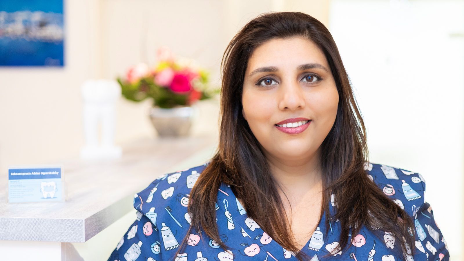 Eine Frau in einem blauen OP-Kittel lächelt in die Kamera.