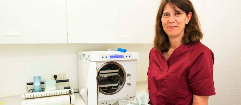 Eine Frau im roten OP-Kittel steht vor einem Autoklaven.
