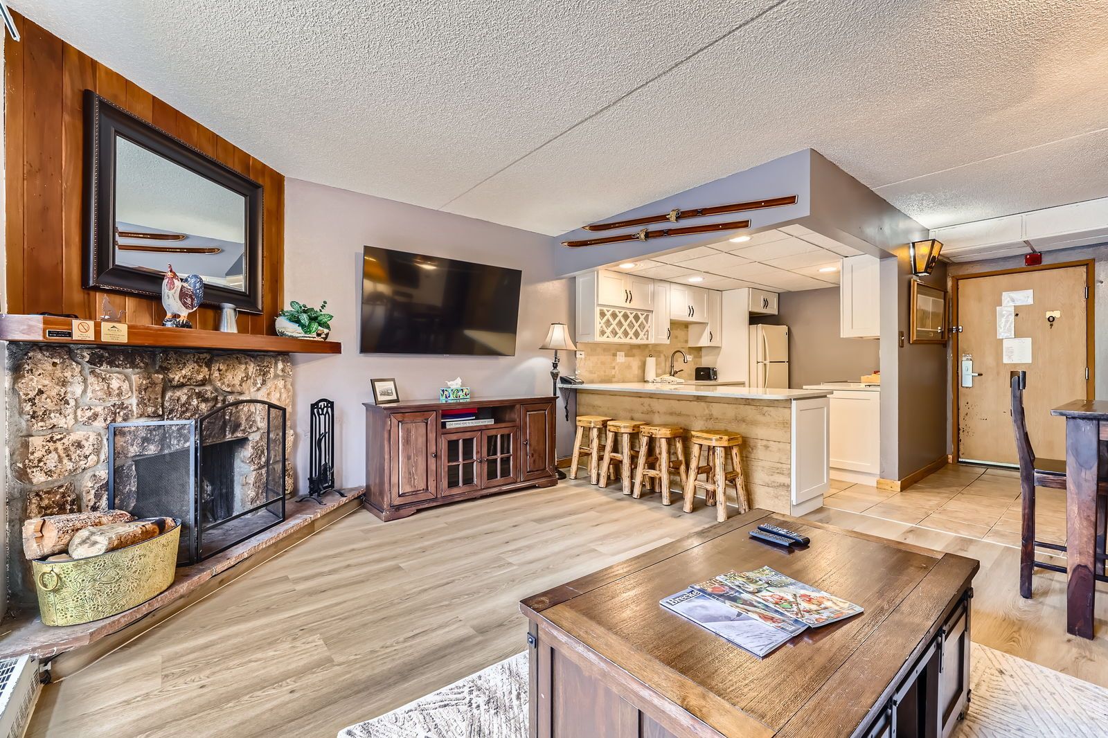 Living room with fireplace, kitchen, TV, and wooden furniture.