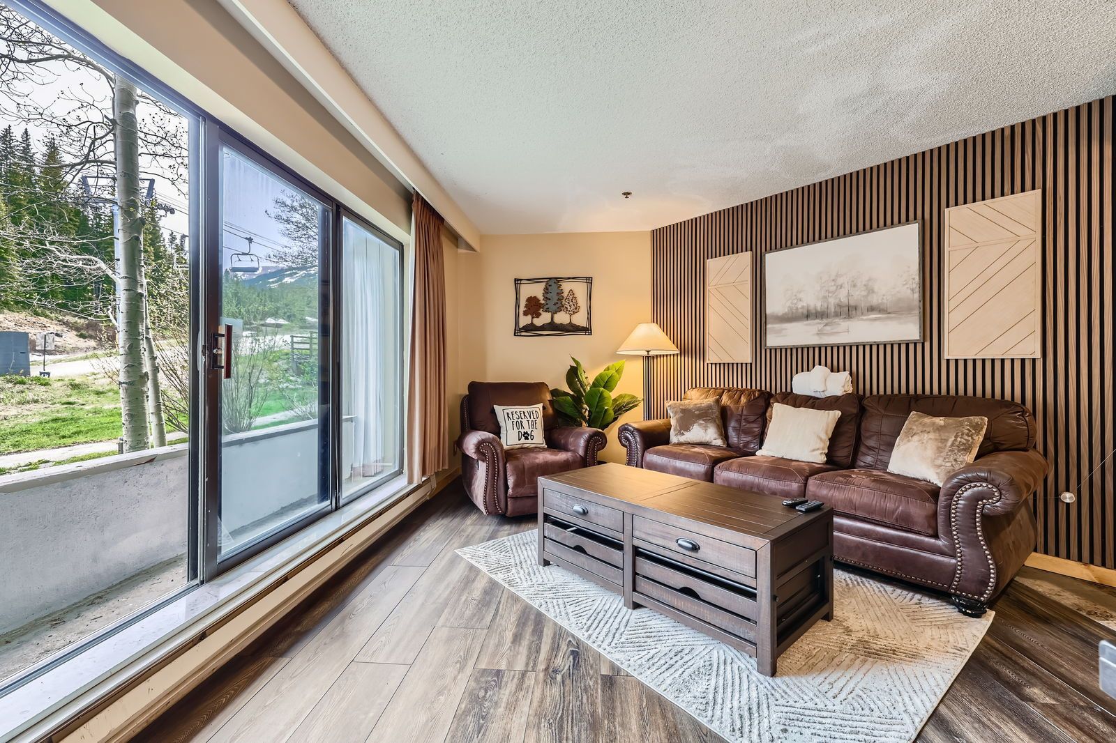 Living room with brown leather furniture, sliding glass door, and decorative wall panels.