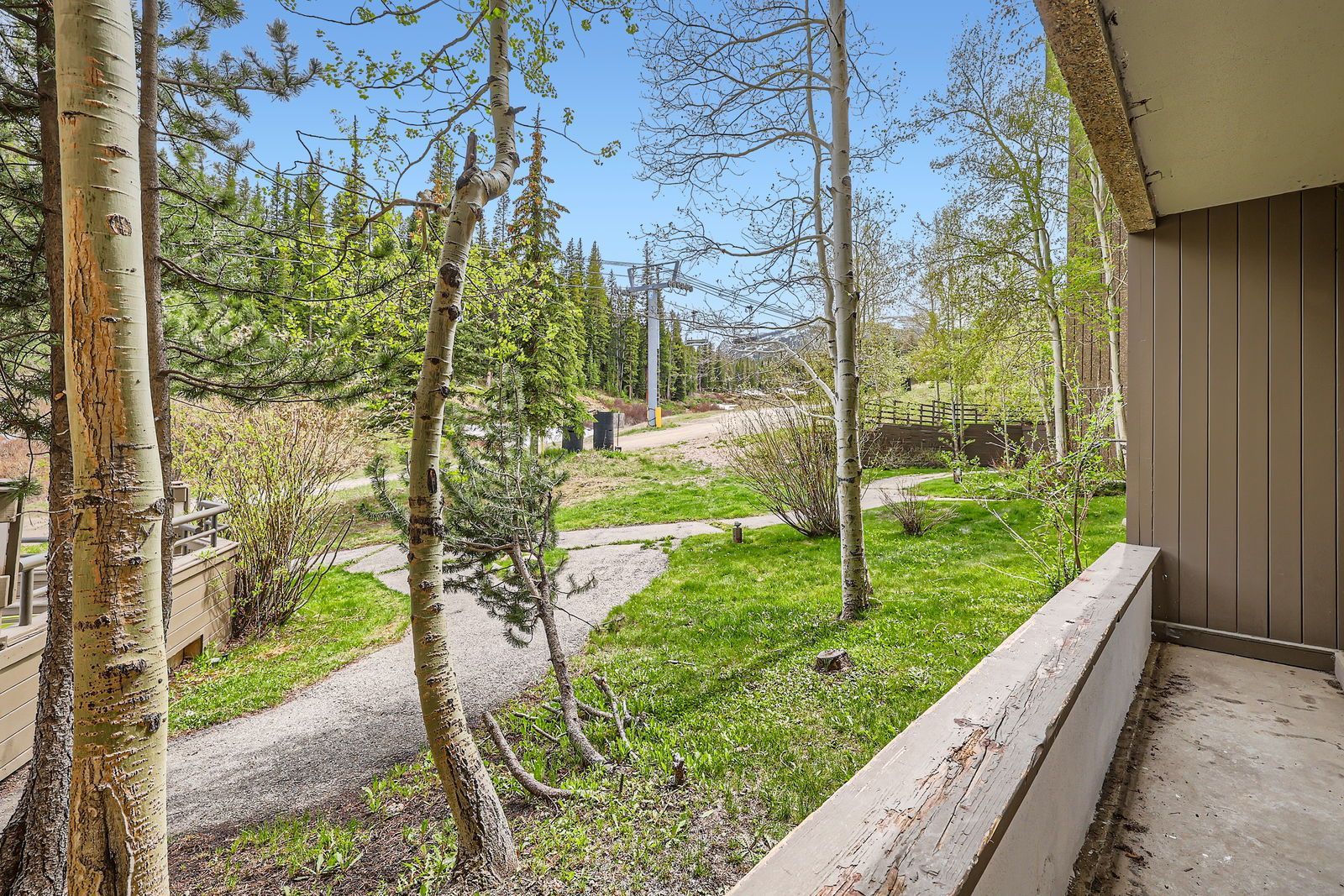 Balcony view: trees, green grass, walking path, lift tower in background.