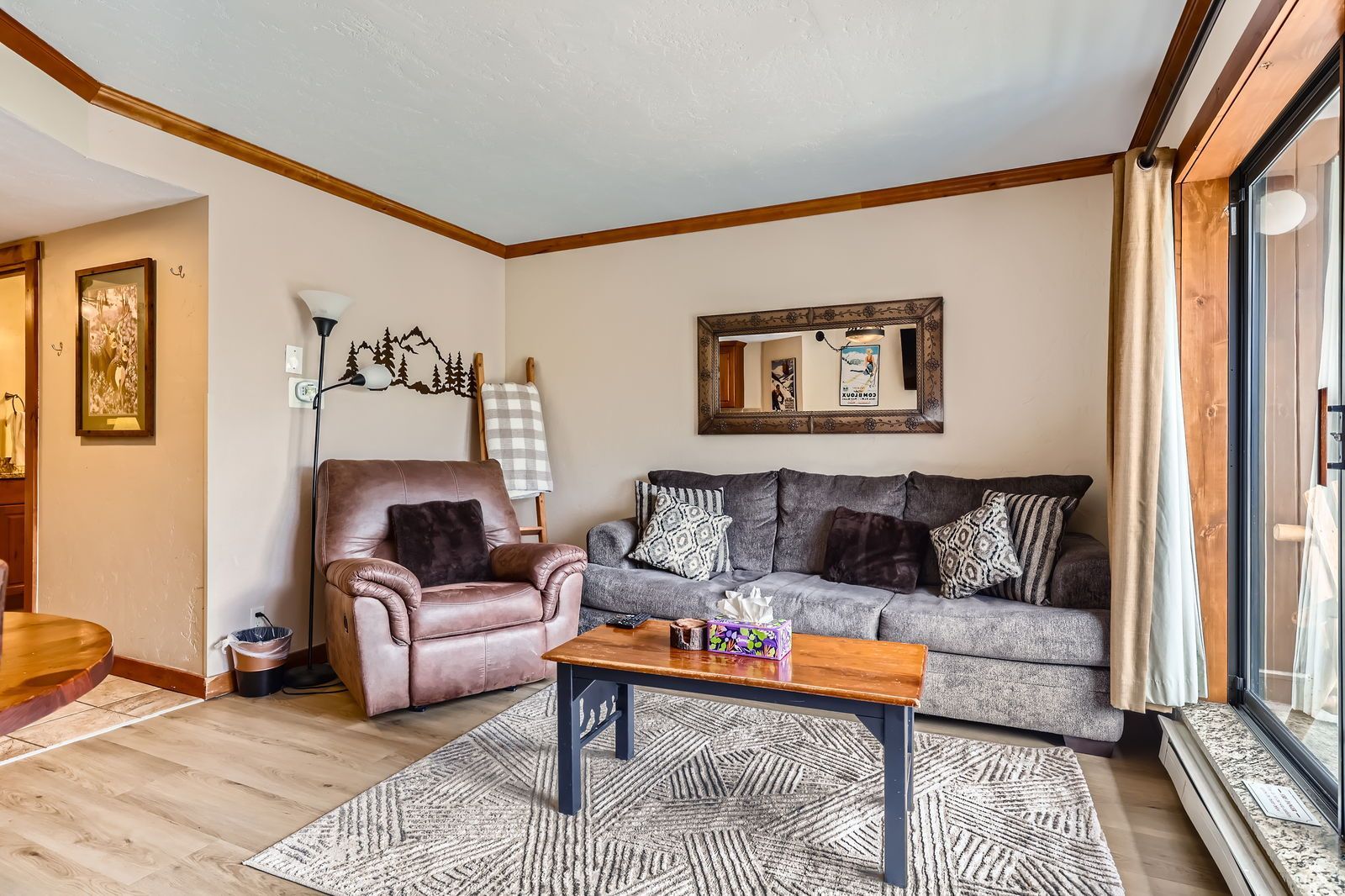 Living room with brown leather recliner, gray couch, wooden coffee table, and large window.