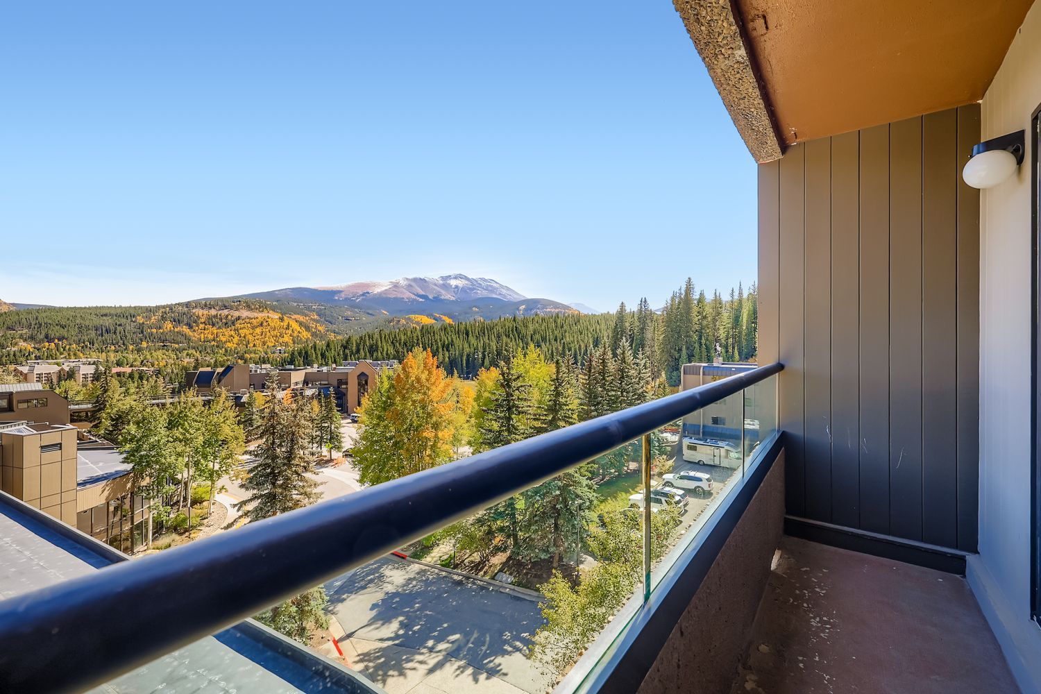 Balcony with glass railing overlooking a mountain landscape with trees and buildings.