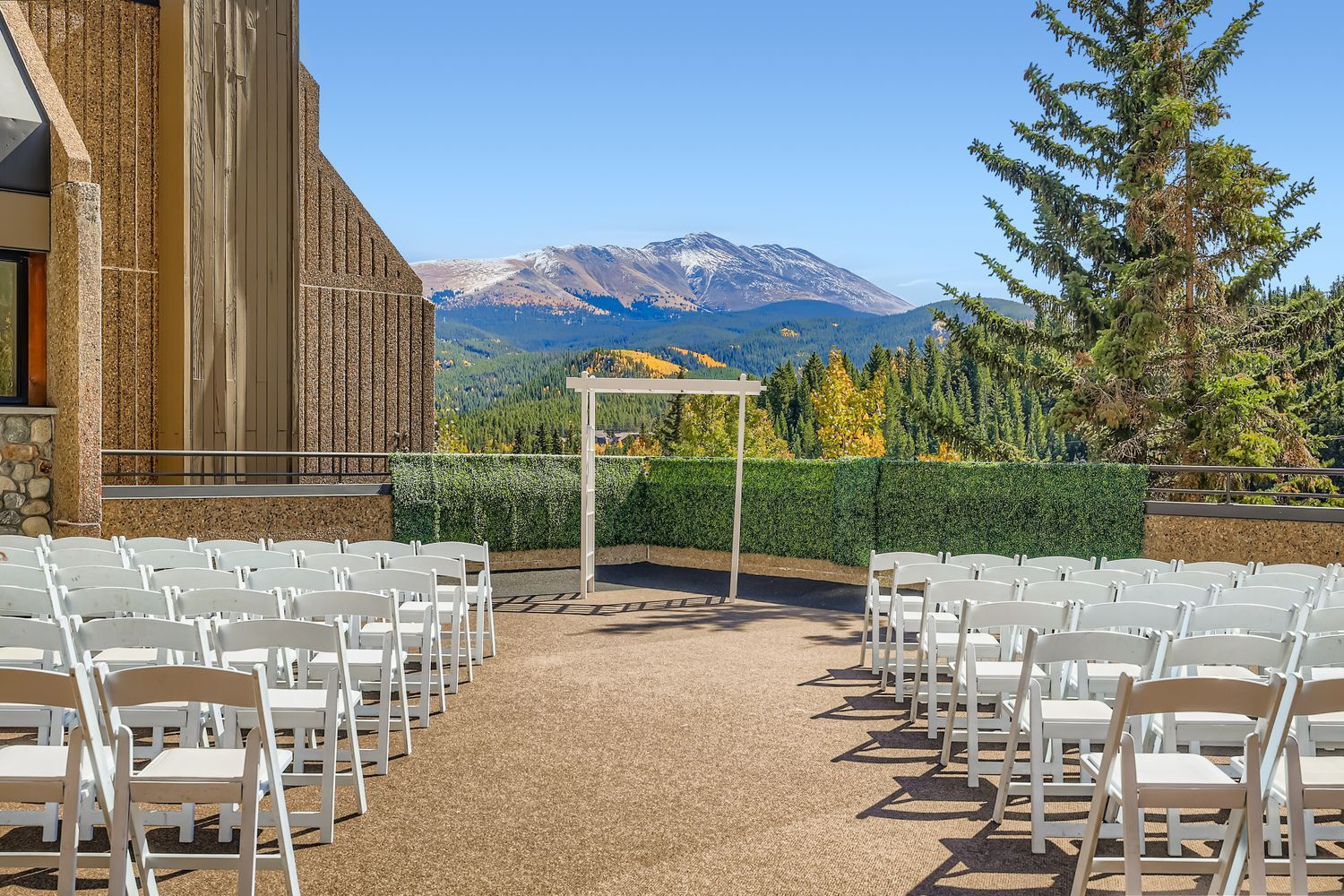 Outdoor wedding ceremony setup with white chairs, arch, and mountain backdrop.