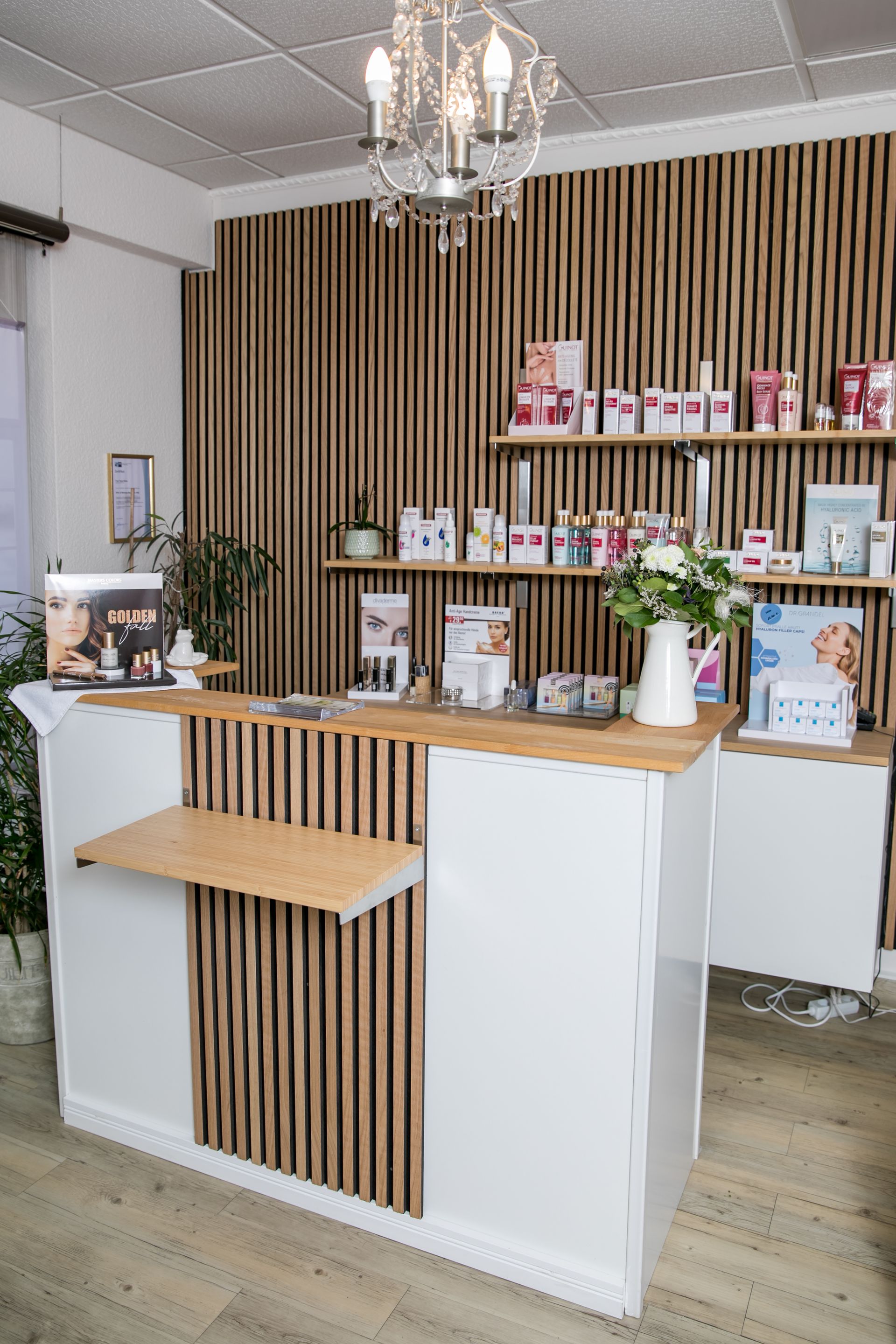 Empfangstresen in einem Spa mit Akzenten aus Holzlatten, weißen Schränken und Produktausstellungsregalen vor einer Holzwand.