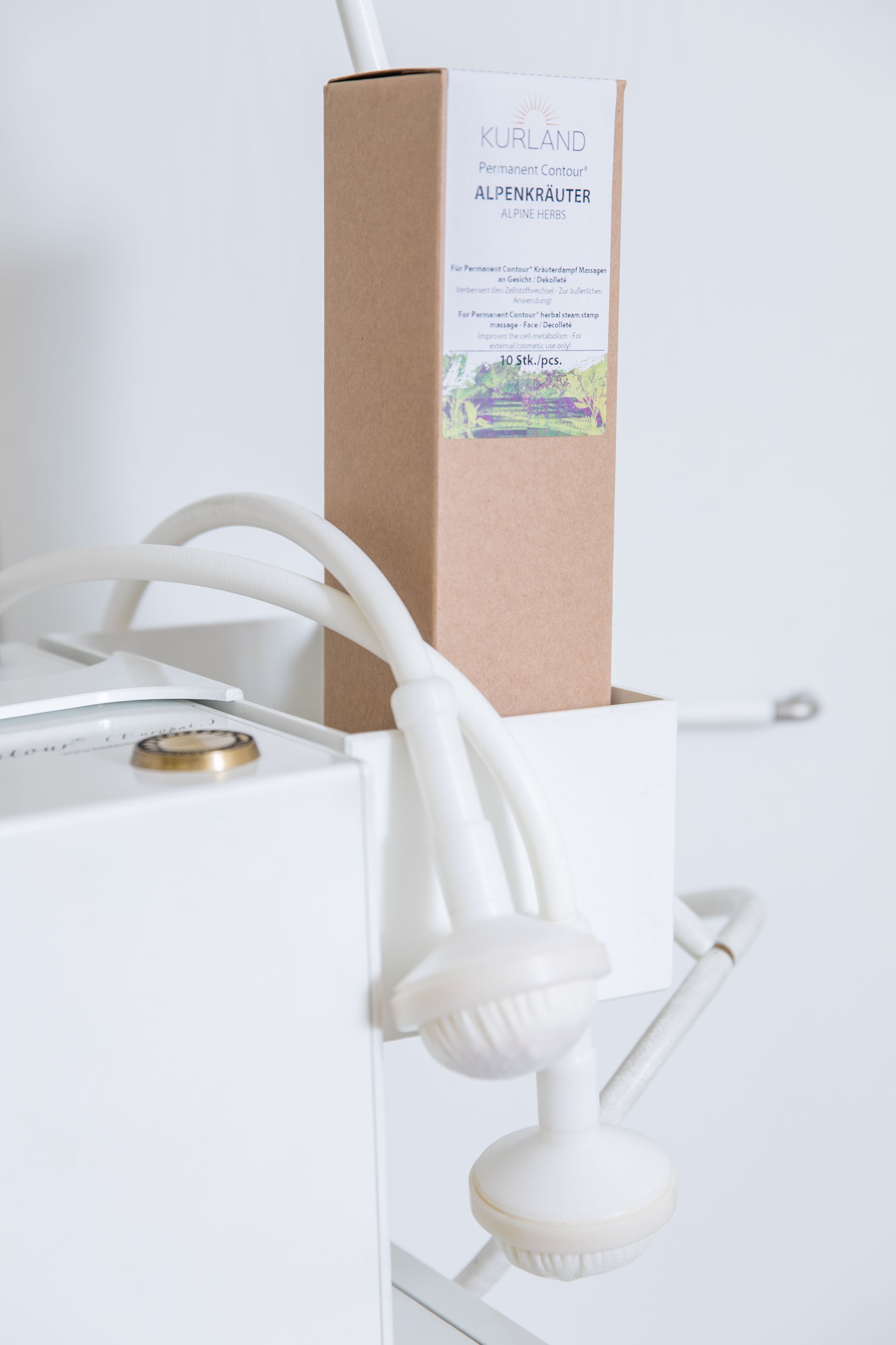 Ein weißer Duschkopf und eine braune Box mit Text stehen auf einer weißen Struktur in einem weißen Badezimmer.